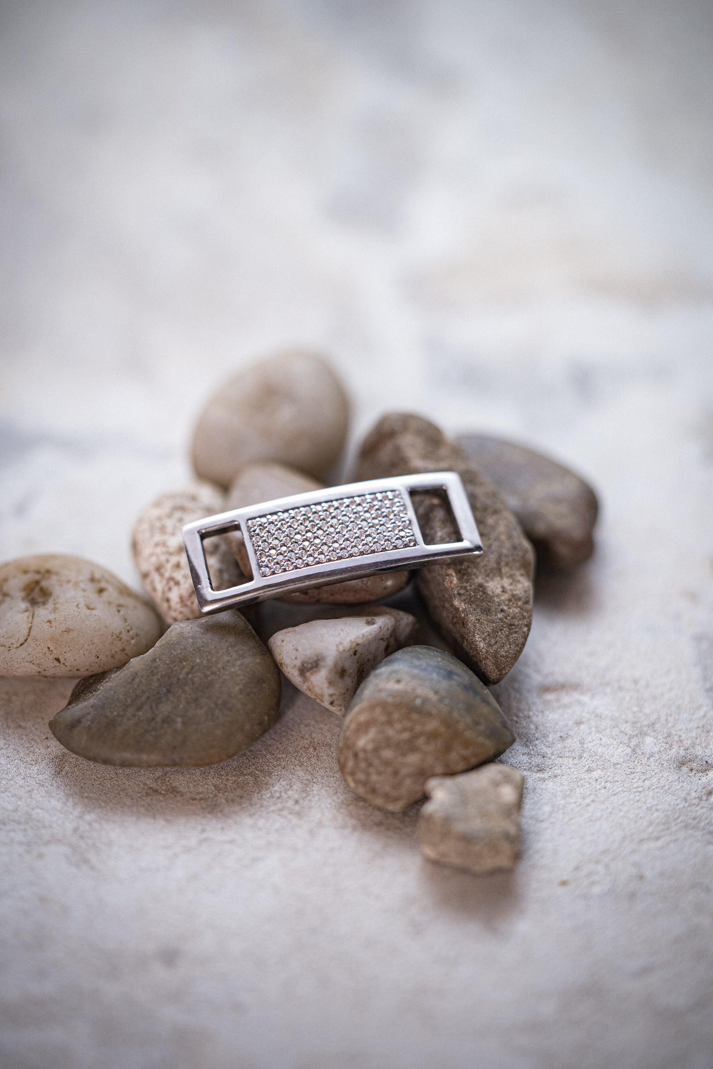 Silver bracelet with embedded stones resting on a collection of small rocks.