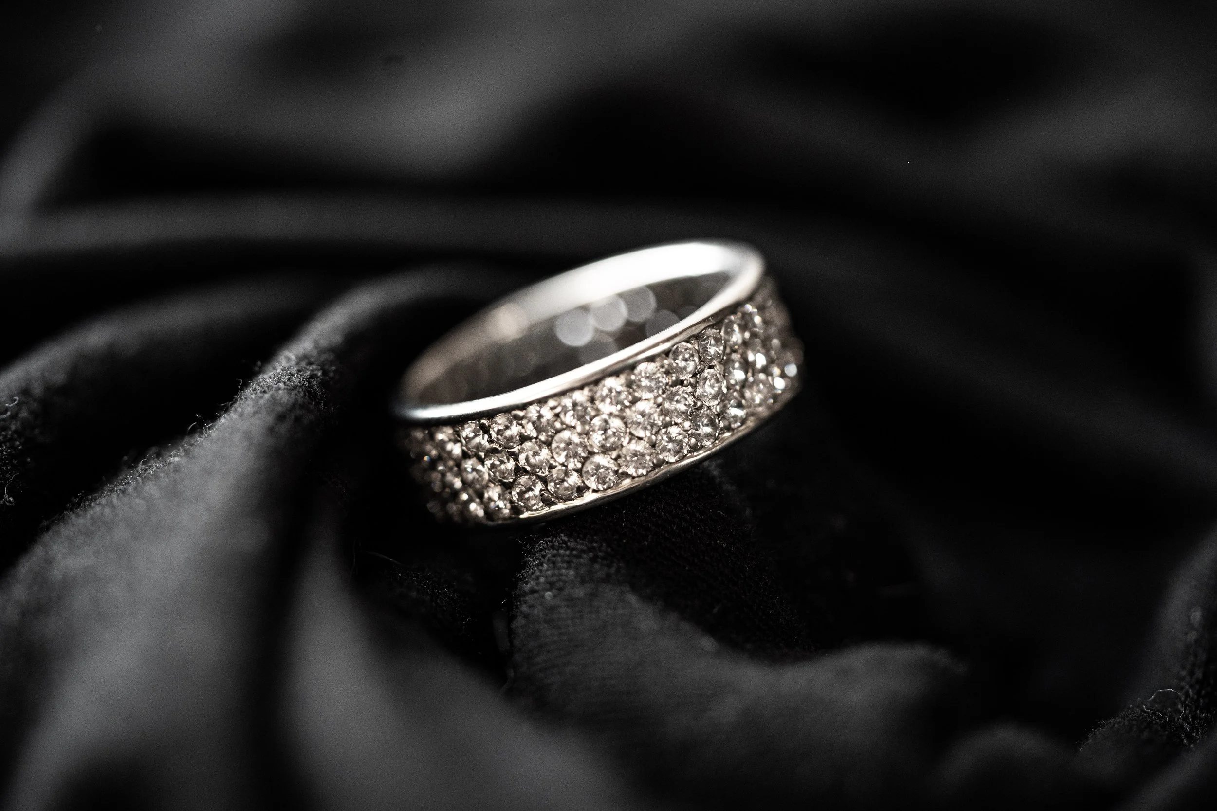A silver ring encrusted with multiple small diamonds resting on black fabric.