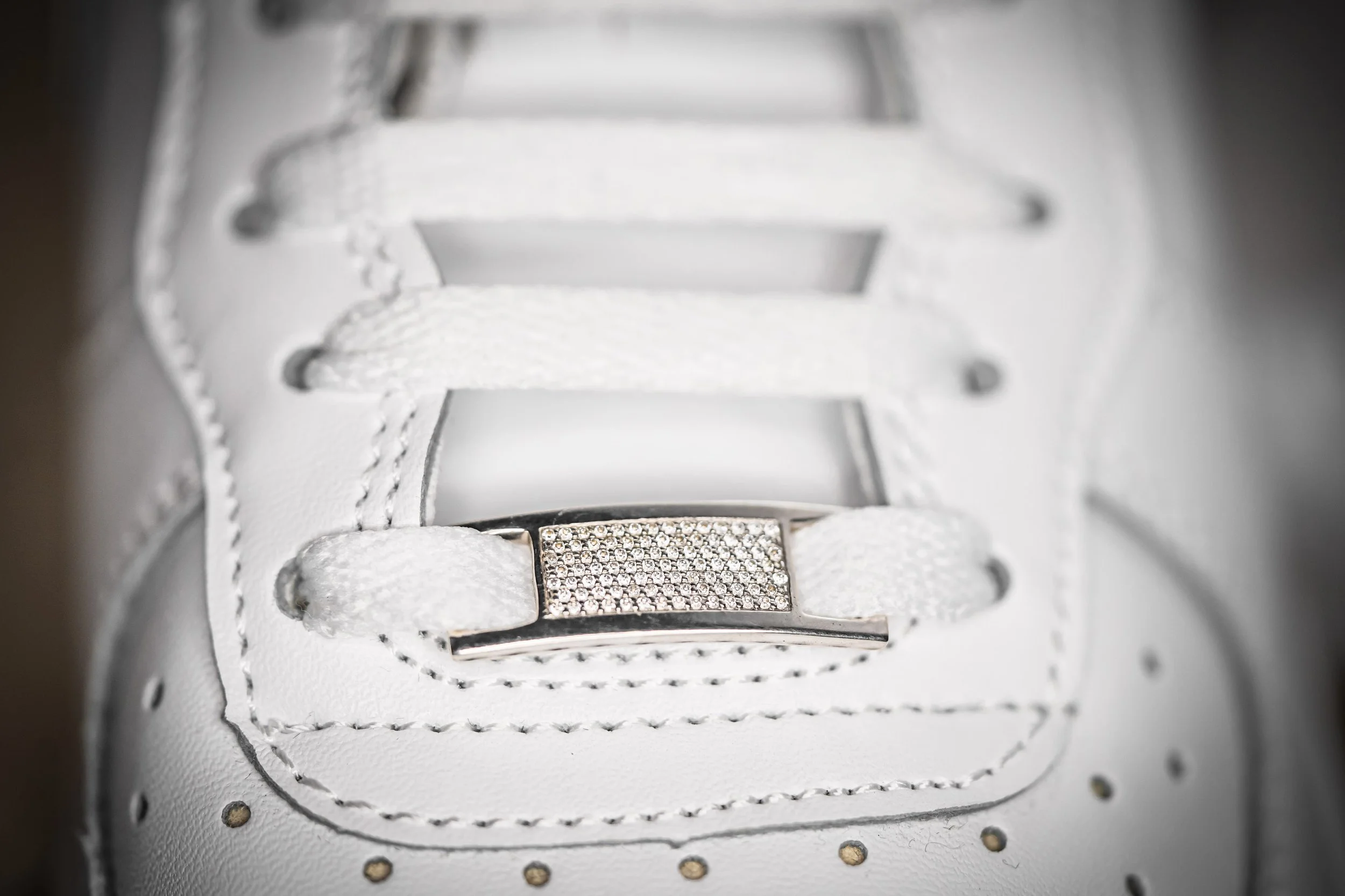 Close-up of a white sneaker with a rectangular metallic lace tag encrusted with small rhinestones.