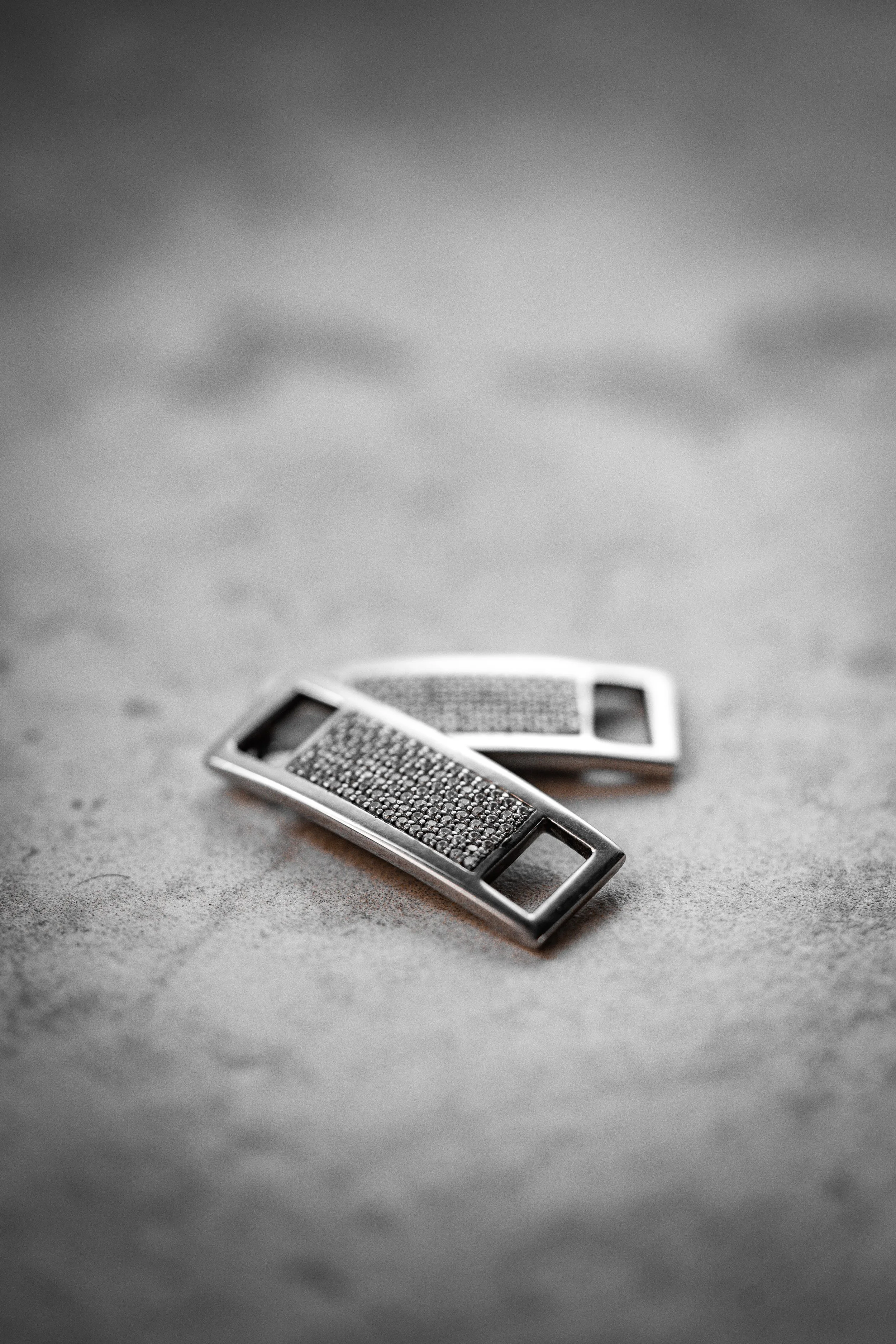 Close-up of two rectangular belt buckle clasps with embedded small crystals, lying on a textured surface.