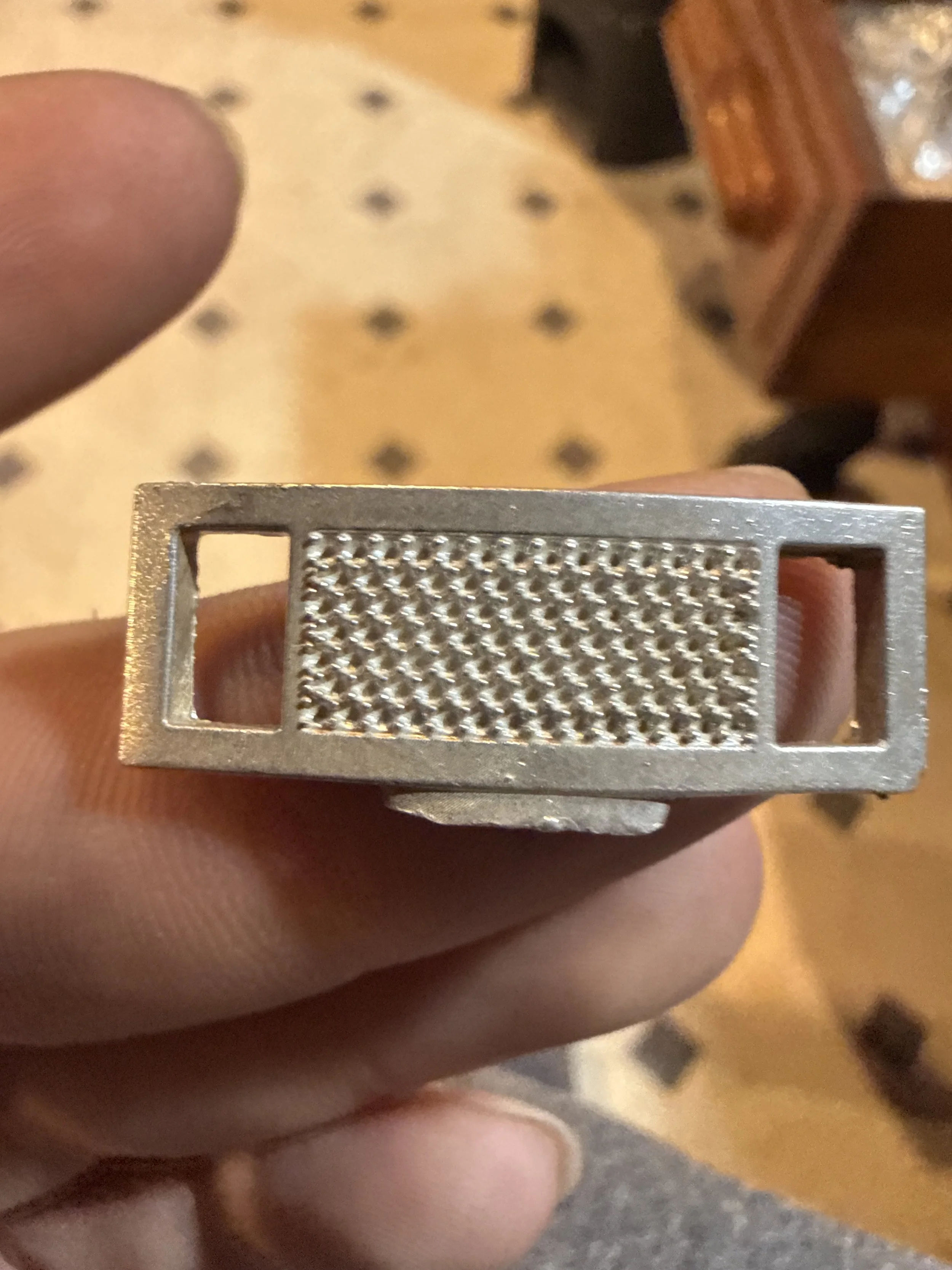 Close-up of a metallic object with a textured center and two rectangular cutouts on either side, held between fingers.