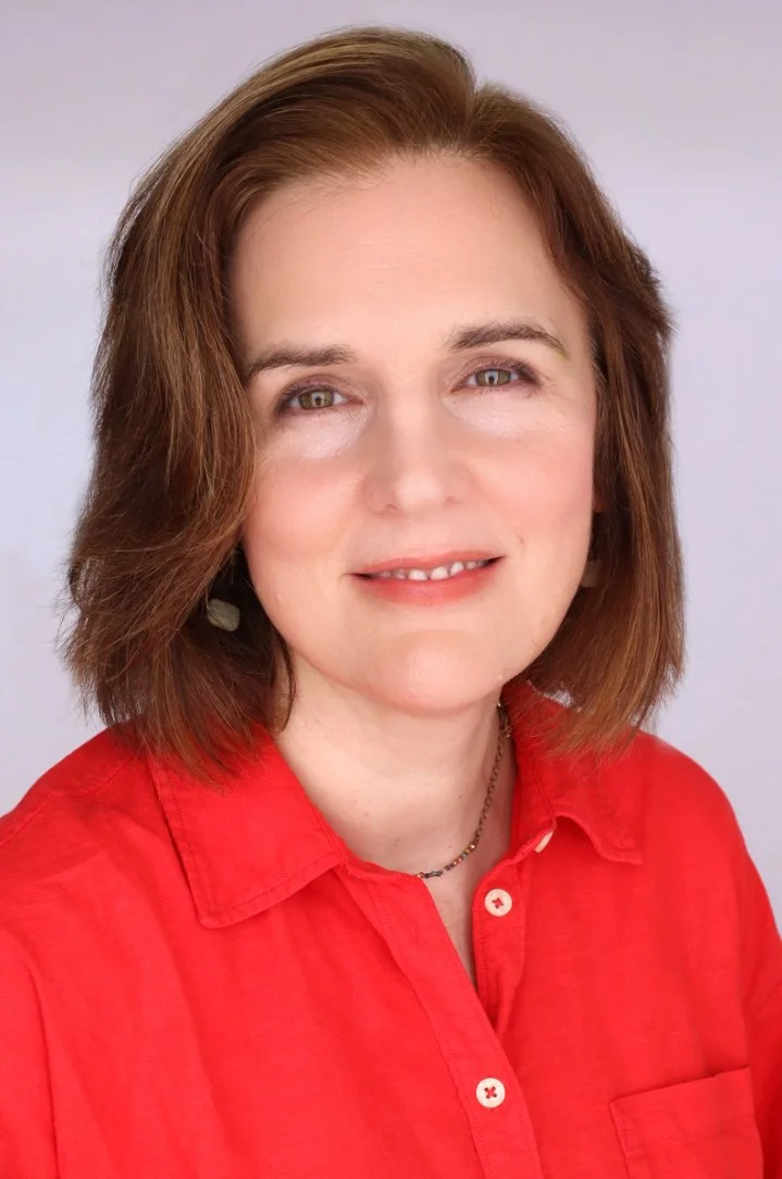 A woman with shoulder-length brown hair, wearing a red button-up shirt and a necklace, smiling against a plain light background.