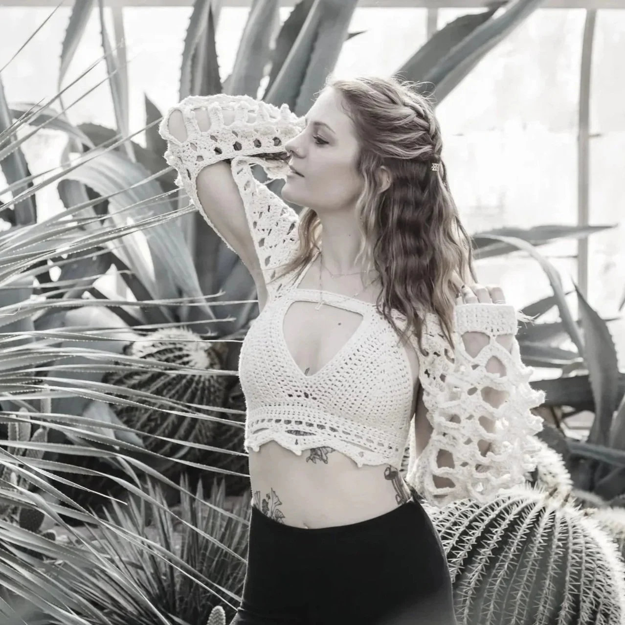A woman with wavy hair posing in front of large desert plants inside a greenhouse.