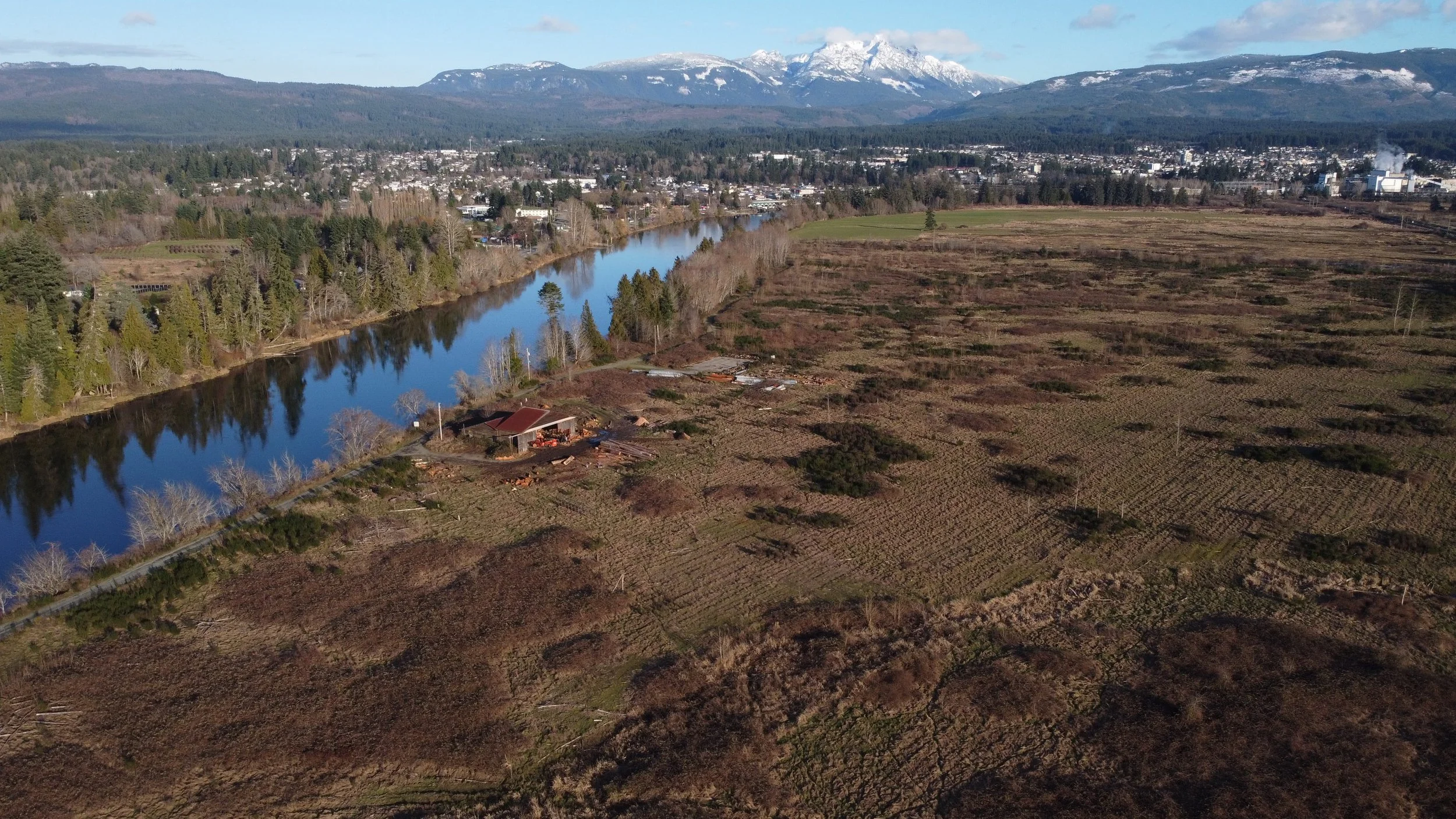 Aerial view of a river flowing through a valley with a city and snow-capped mountains in the background.
