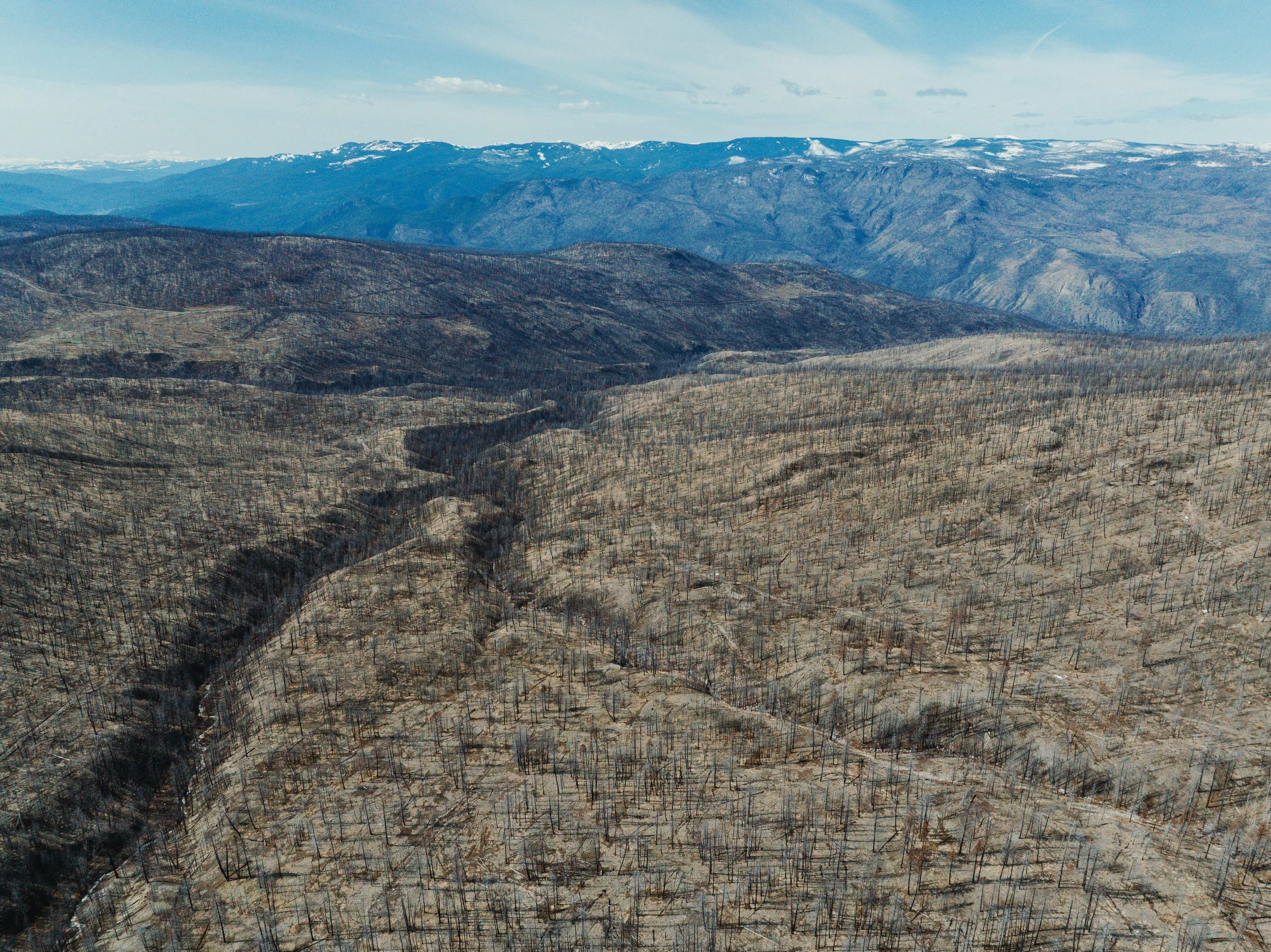 Aerial view of a mountain landscape with burned trees and a winding river through a dry, barren area.
