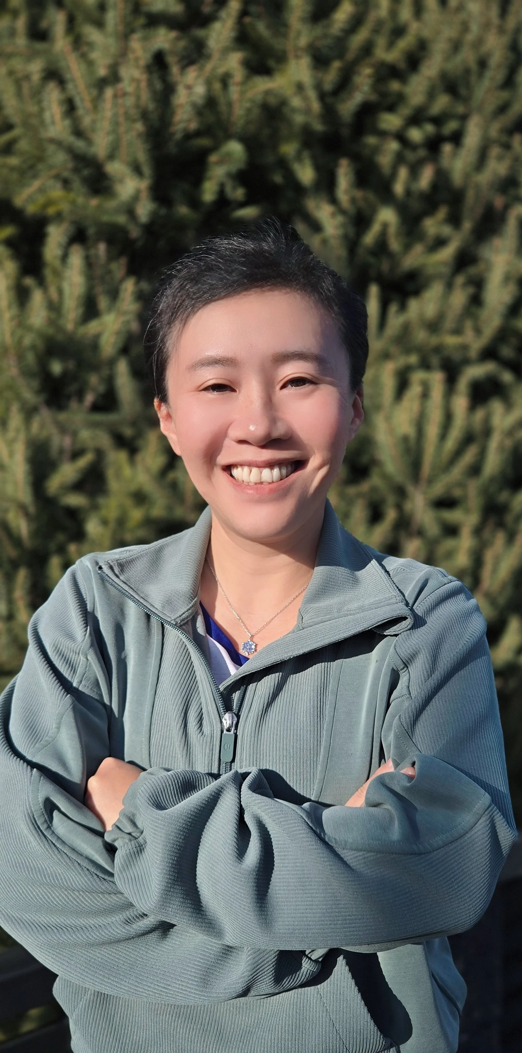 Erin Yang, Cariboo Carbon Solutions Officer Manager, smiling outdoors with her arms crossed, standing in front of tall cactus plants.