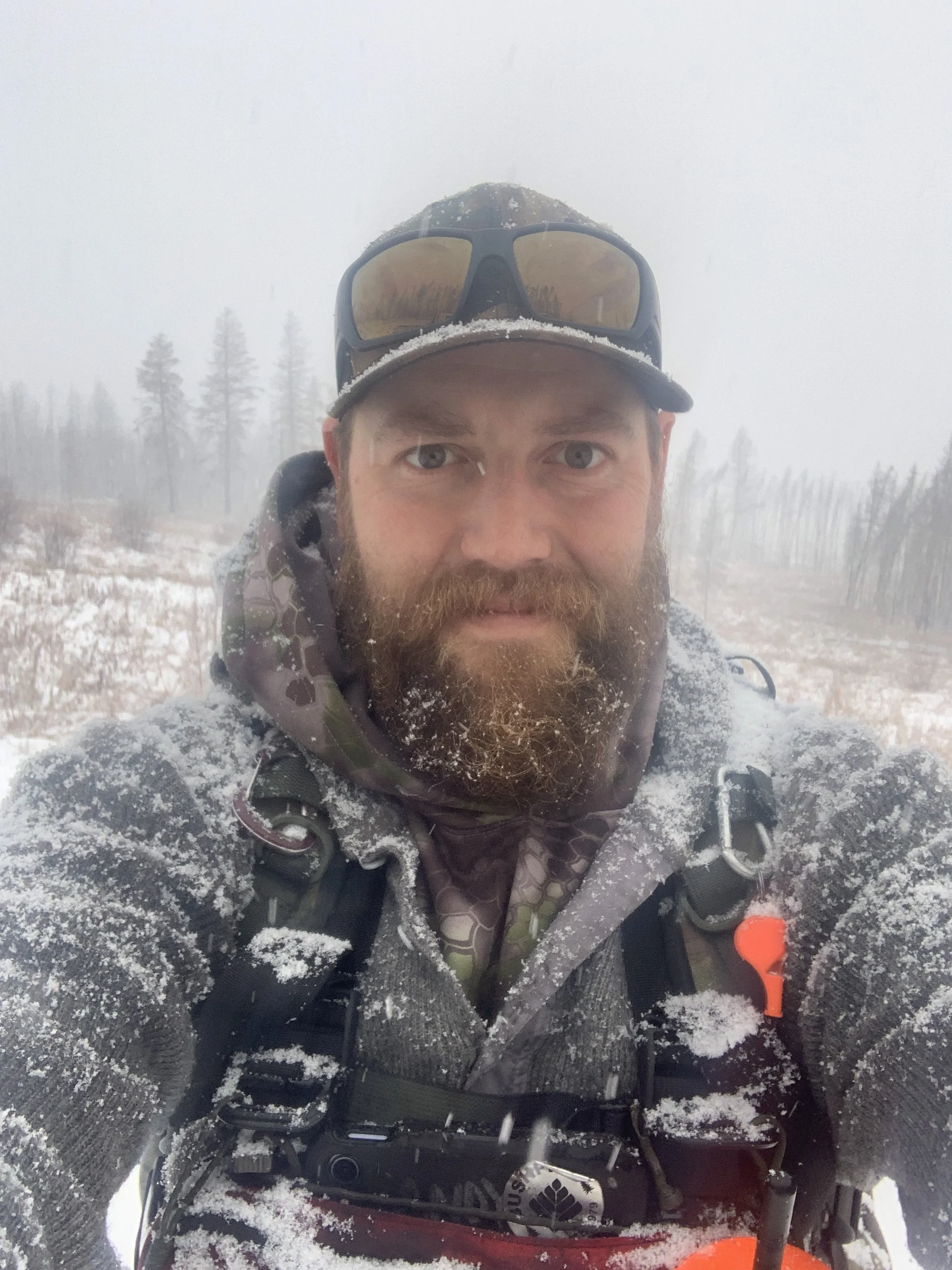 Andy Belicka in winter gear taking a selfie outdoors in snowy and foggy conditions, wearing a cap, sunglasses, and a backpack.