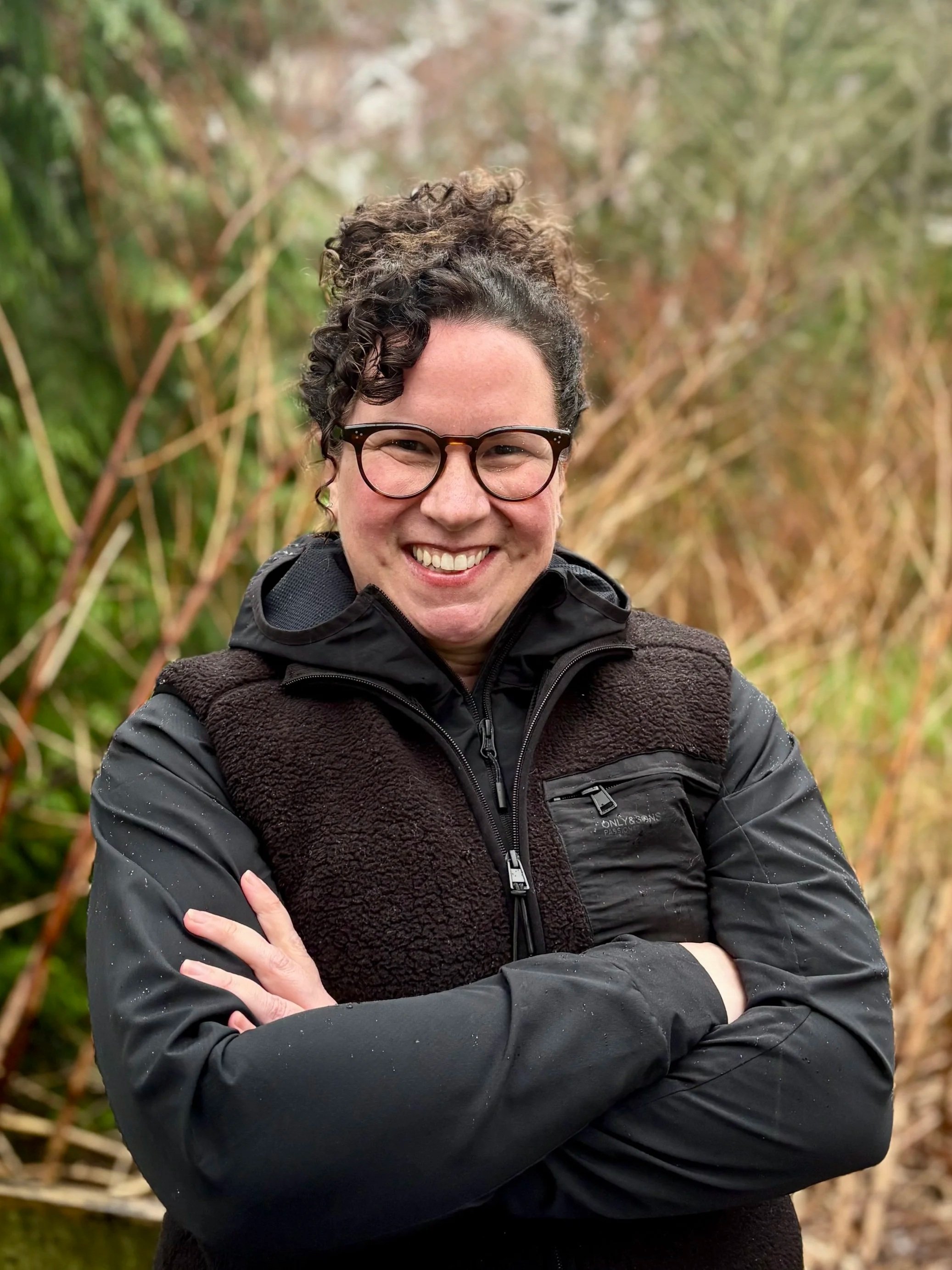 Mia Finn, VP Projects, hair smiling outdoors near water during fall.