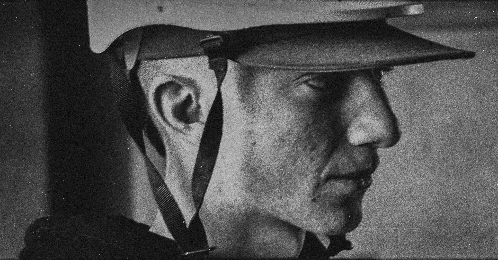 Close-up black and white photo of a man wearing a helmet, depicted in profile with a serious expression.