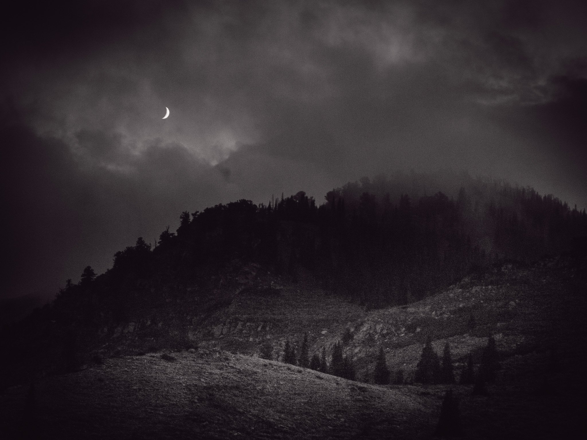 Nighttime landscape with a mountain and cloudy sky, crescent moon visible in the clouds.