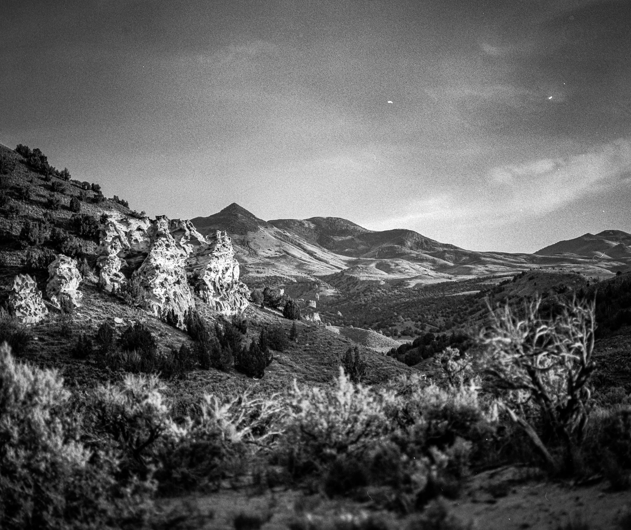 Black and white landscape of hilly terrain with rocky formations and sparse vegetation under a clear sky.