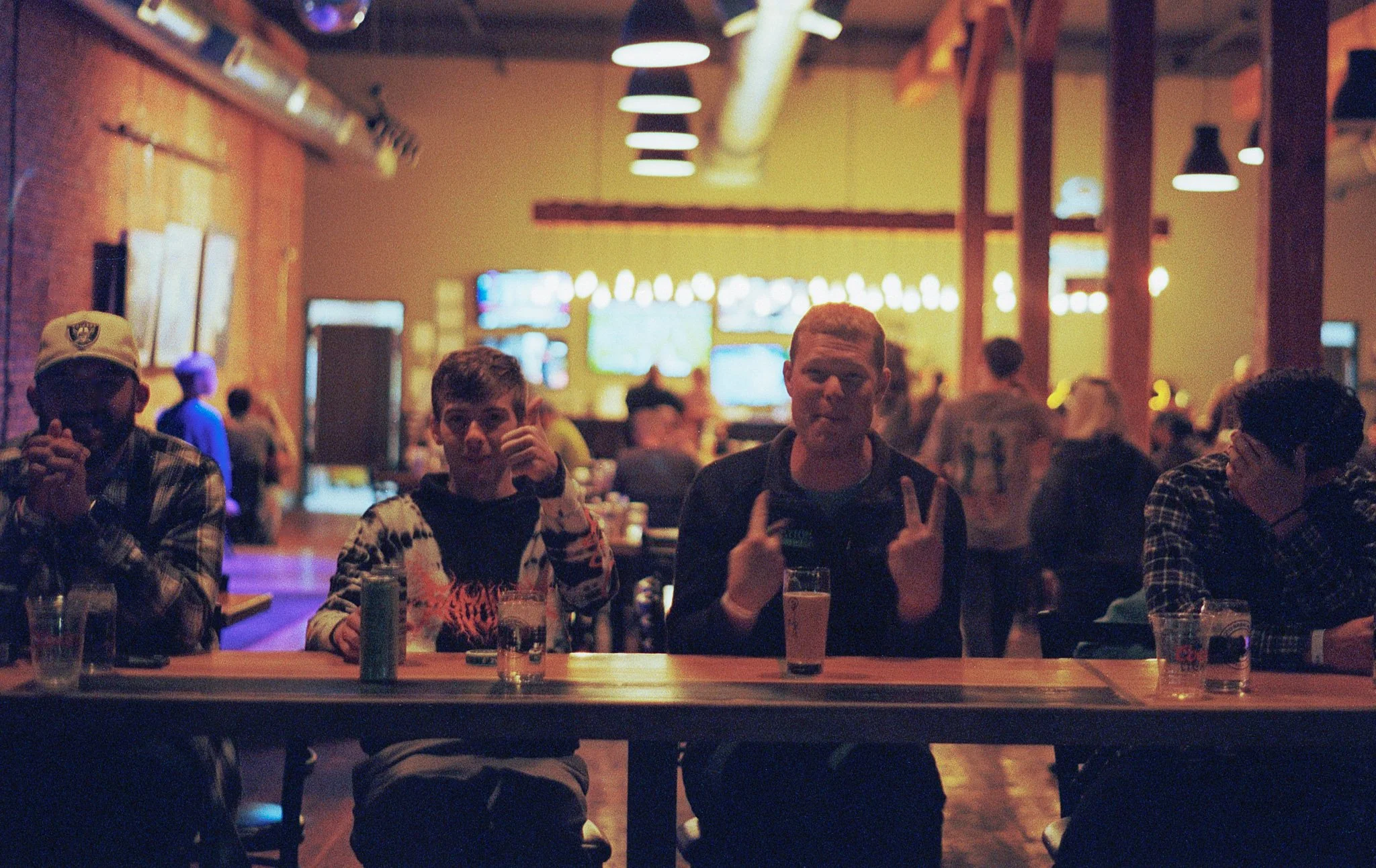 Three people sitting at a bar in a dimly lit sports bar or pub, with several television screens in the background showing sports games.