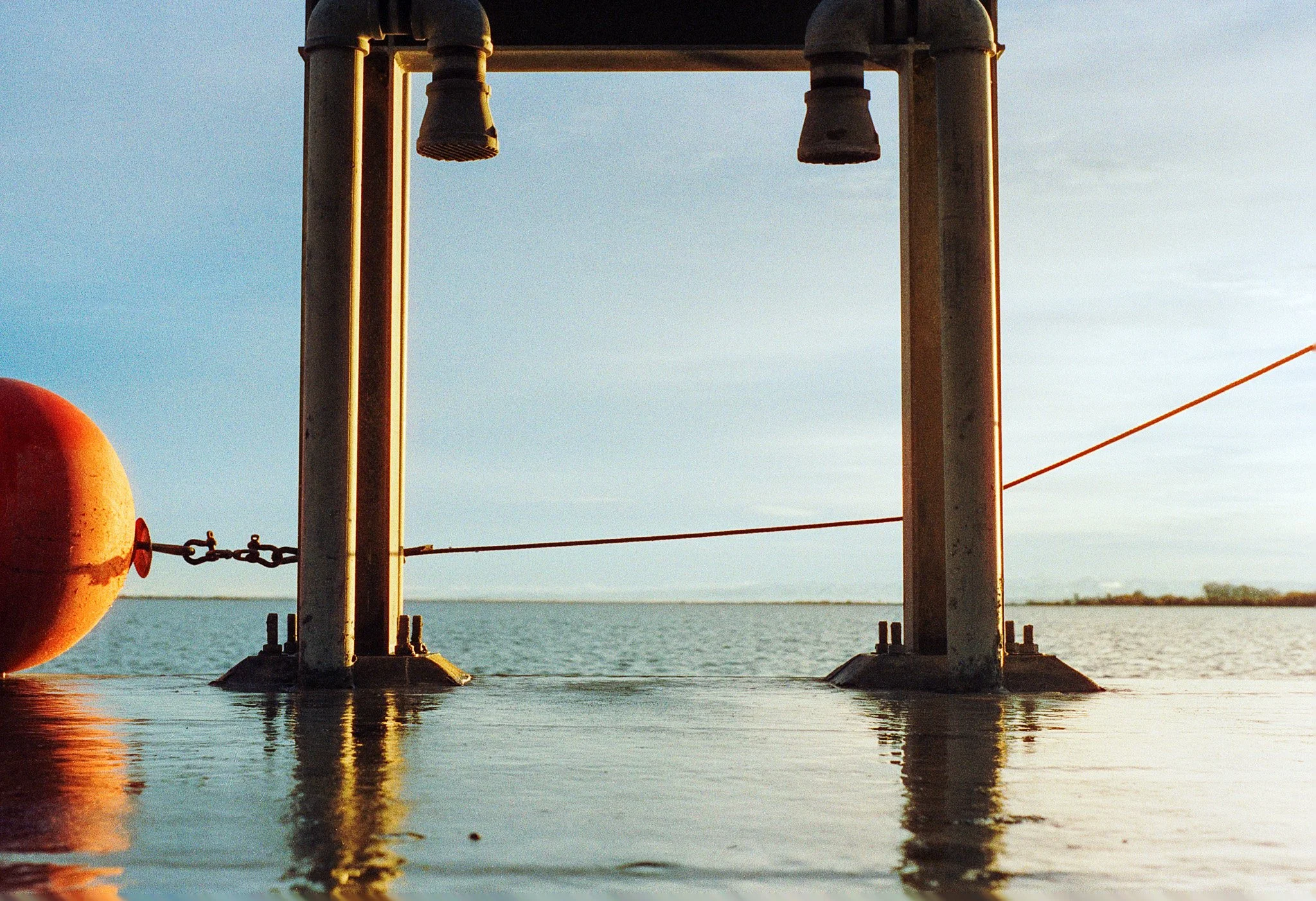 Close-up of a water buoy tethered to a metal pier over a body of water during sunset.