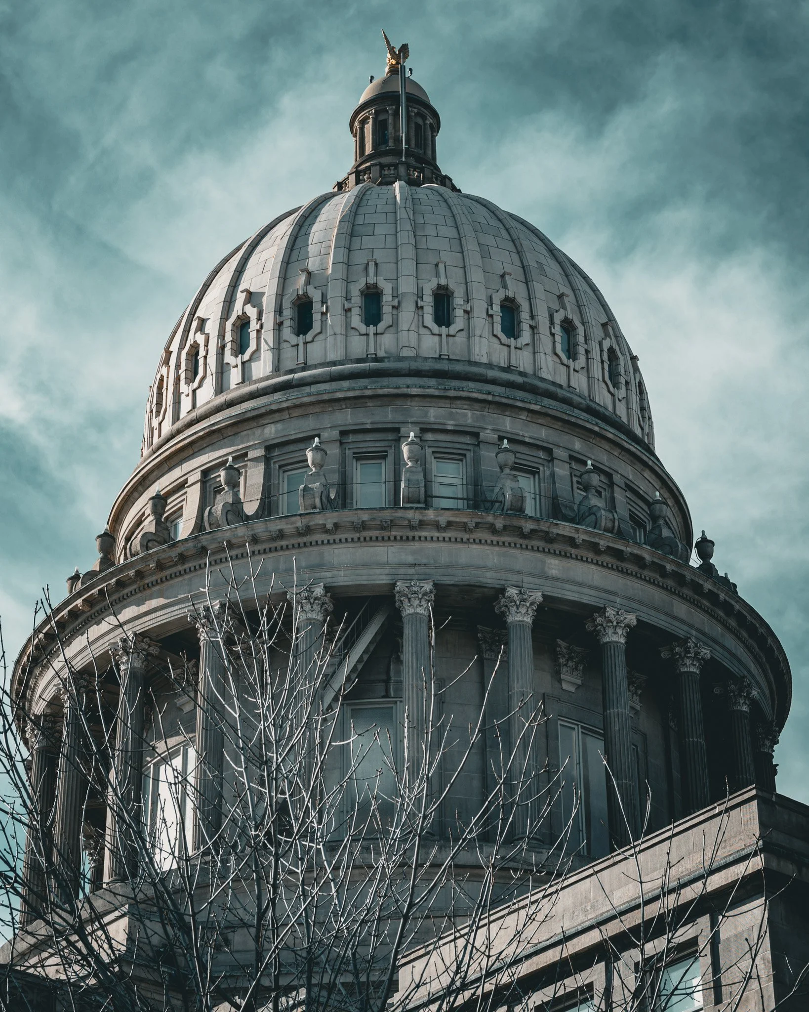 A historical building with a large, ornate dome topped with a statue, columns, and architectural details, set against a cloudy sky.