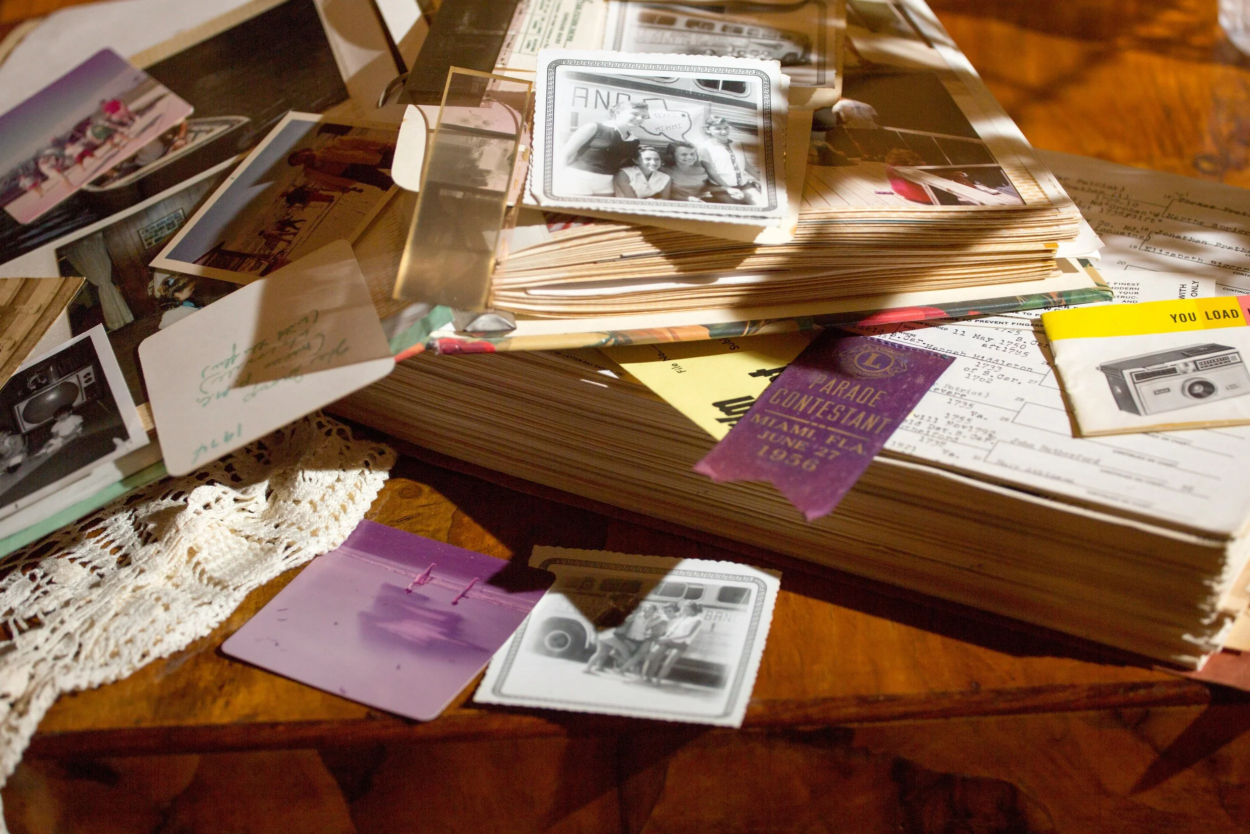 A cluttered wooden table holding old photographs, photo albums, and other keepsakes including a parade ribbon.