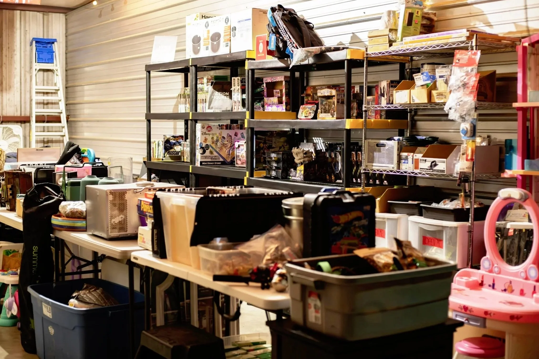 A cluttered garage containing shelves and tables filled with various items including toys, books, and household objects.