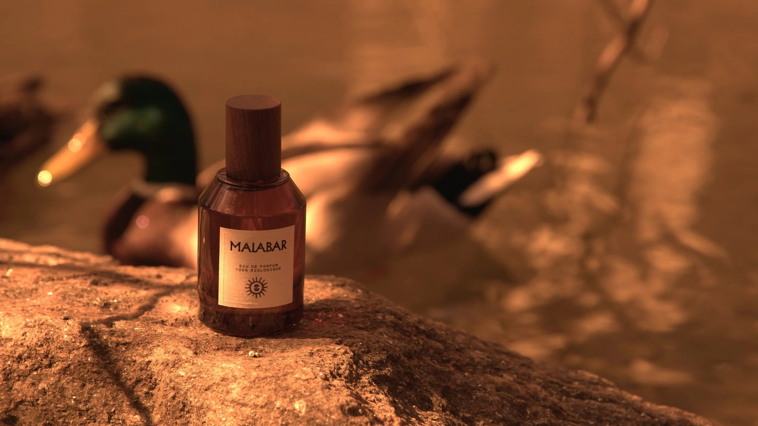 A bottle of Malabar perfume placed on a textured surface in a warm, dimly lit setting with out-of-focus background elements.