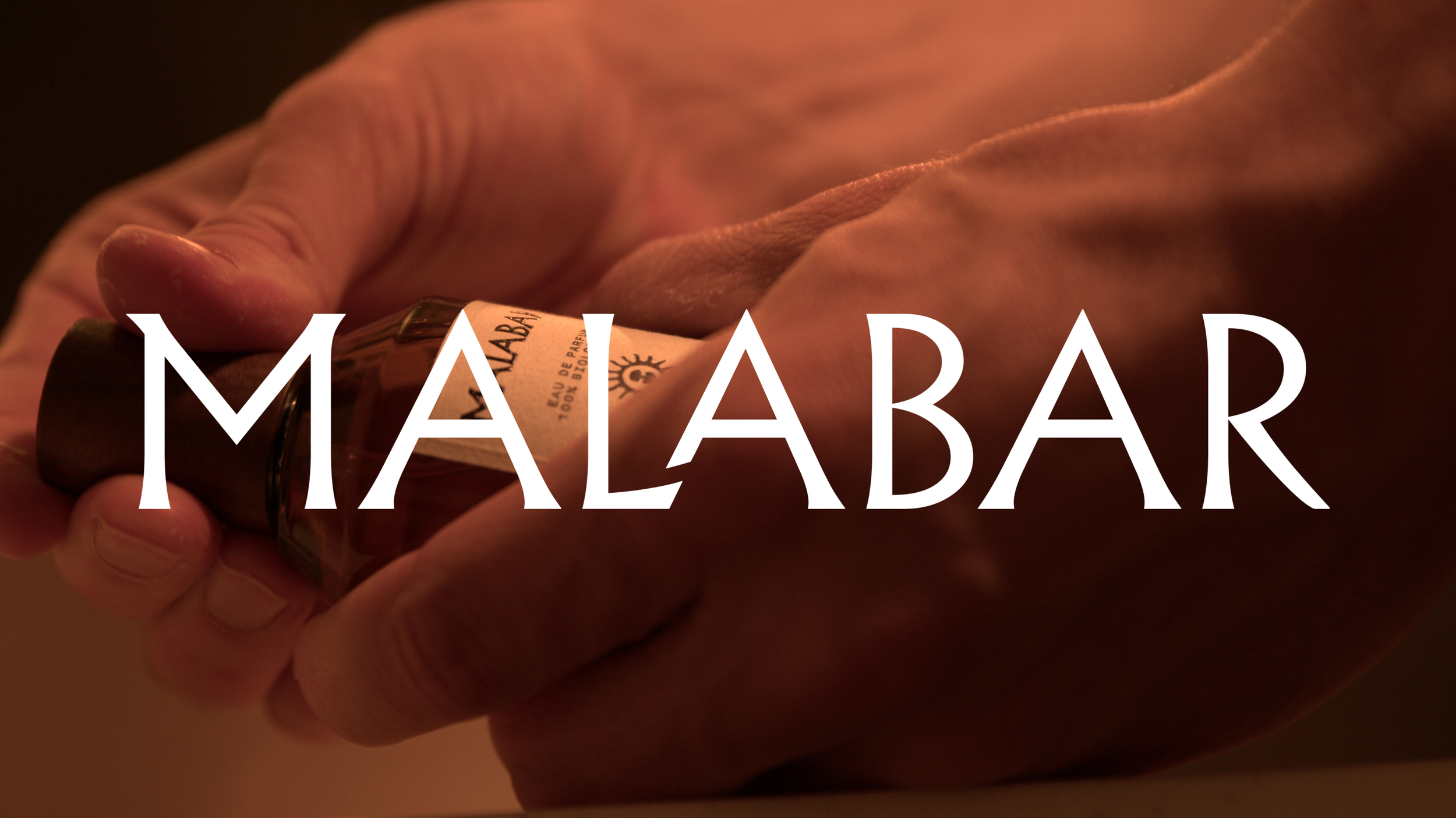 Close-up of a hand holding a small bottle of perfume with the label visible. Large white text overlay reads 'MAAABAR'.