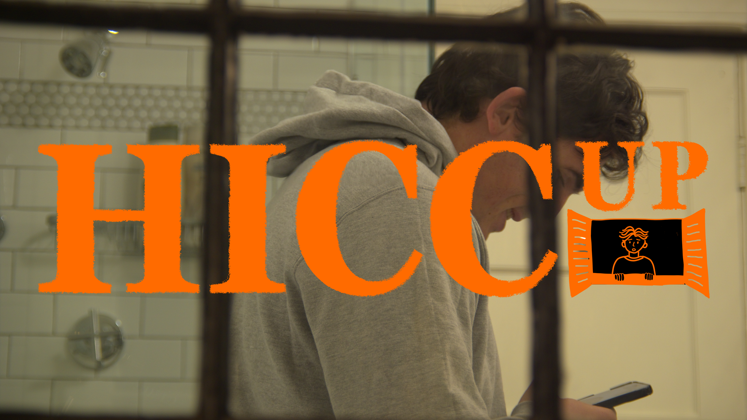 A young man in a gray hoodie leaning forward and looking down at a device, seen through a window with a sign that says 'HICCUP' in large orange letters with a small illustration of a person holding a sign.