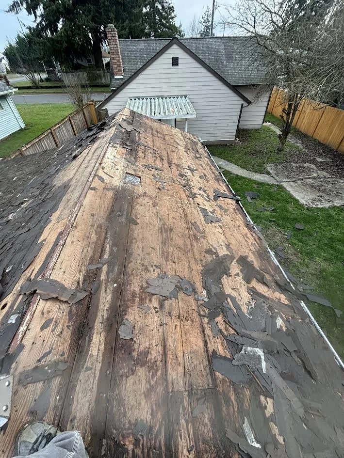 View of a damaged house roof with peeling asphalt shingles, exposing the wood sheathing underneath during roof repair or replacement.