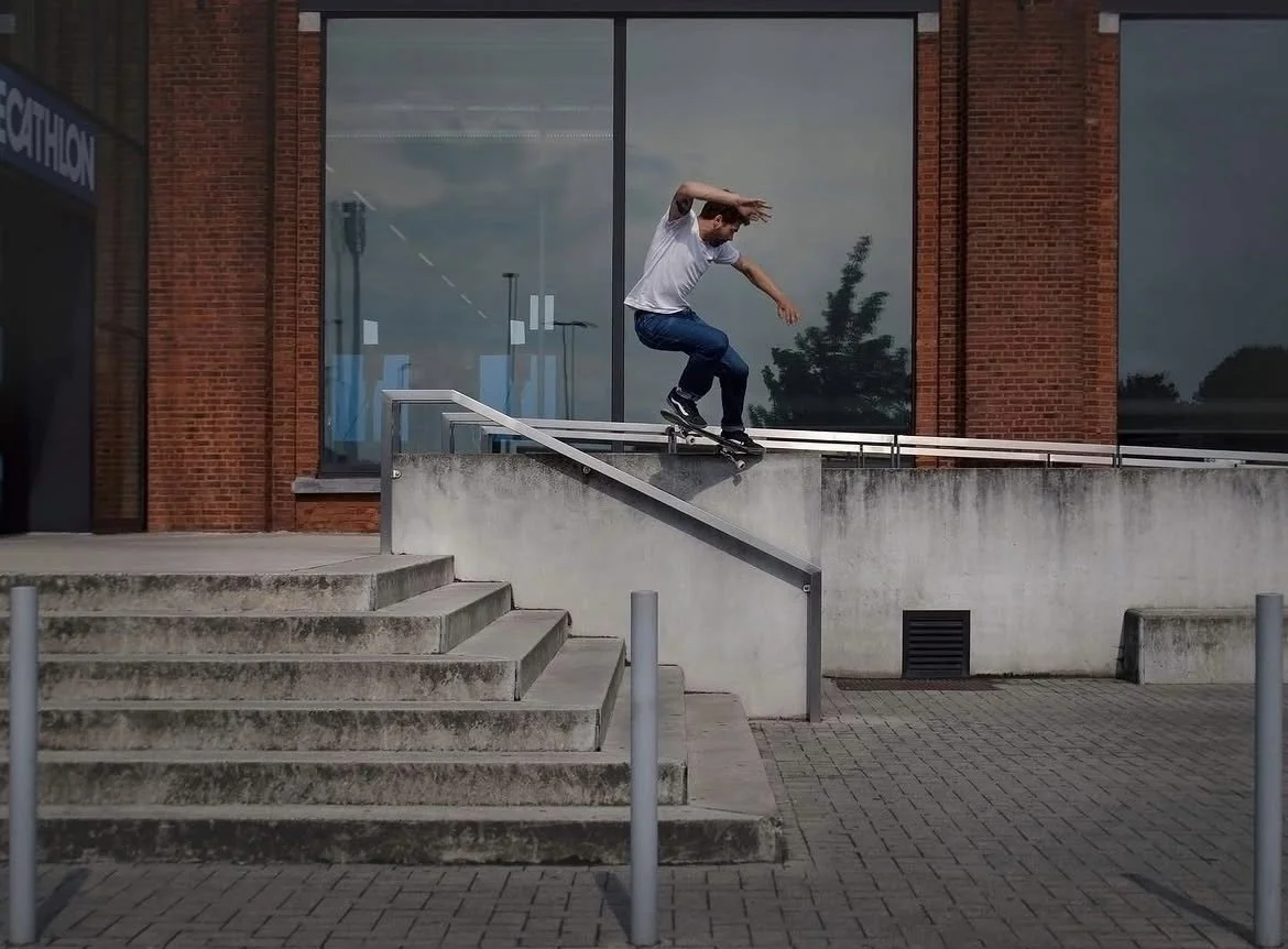 A skateboarder performing a trick on a handrail outside a building with large windows and brick walls.