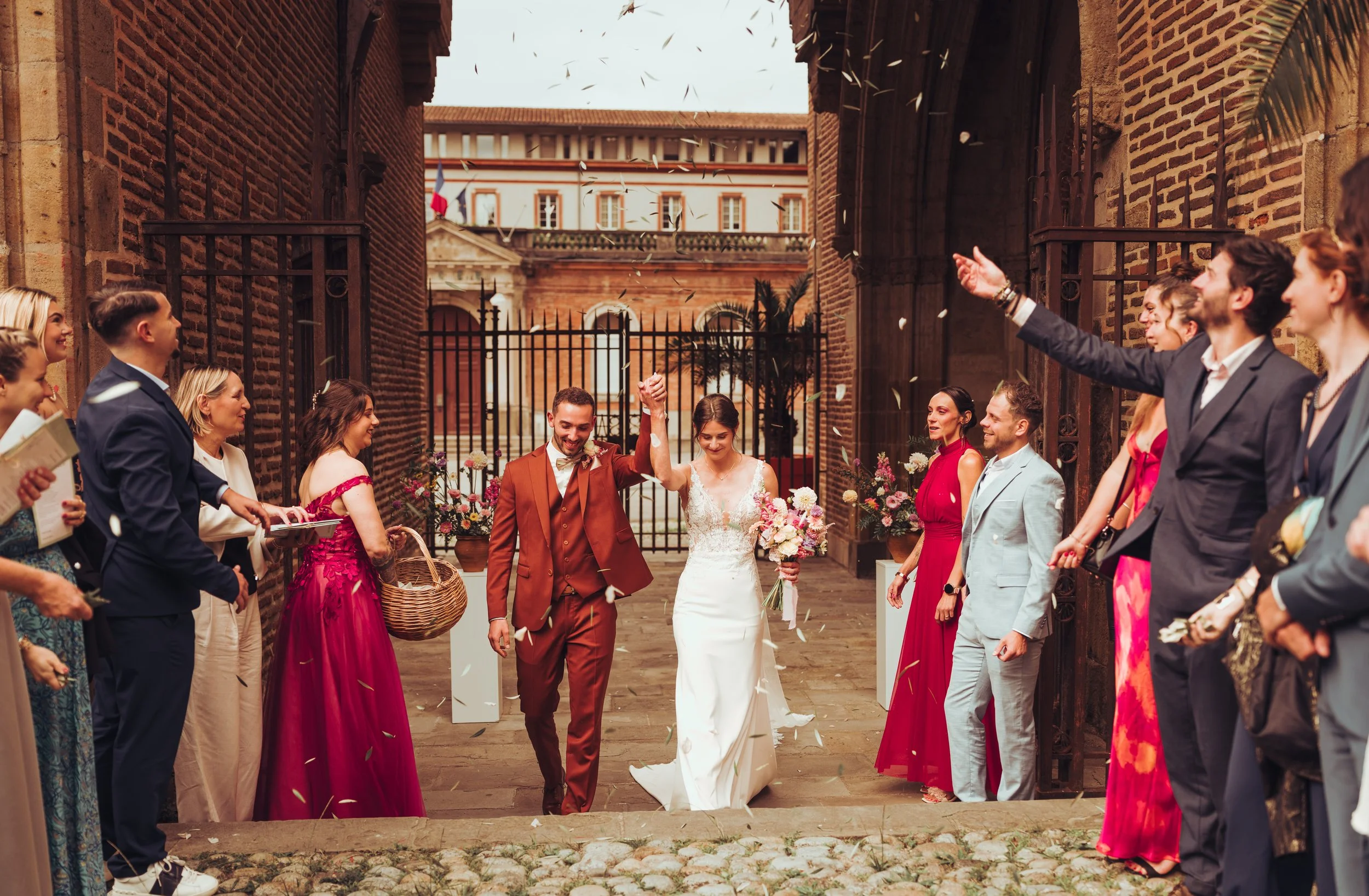 Sortie de cérémonie religieuse dans une cathédrale proche de Toulouse entourée d’amis et de famille lors d’un mariage, avec des fleurs et des invités souriants, en pleine célébration.