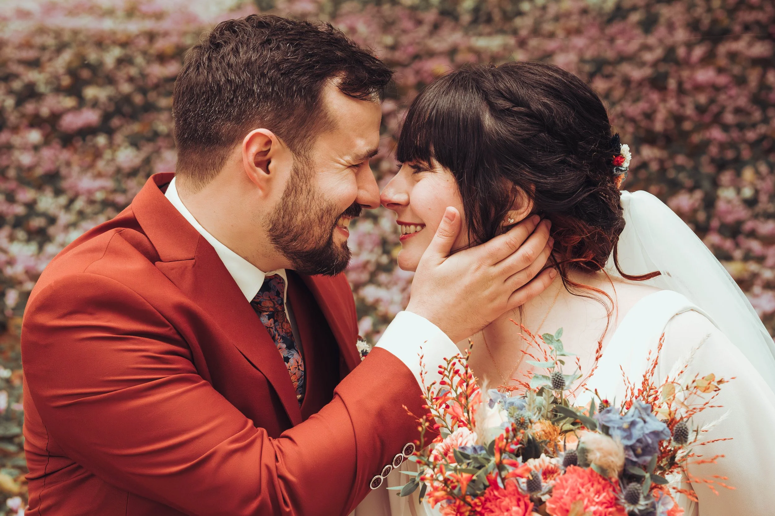 Un couple de mariés au domaine de Gailhaguet proche de Toulouse souriants face à face, dans un champ de fleurs, la femme tenant un bouquet coloré.