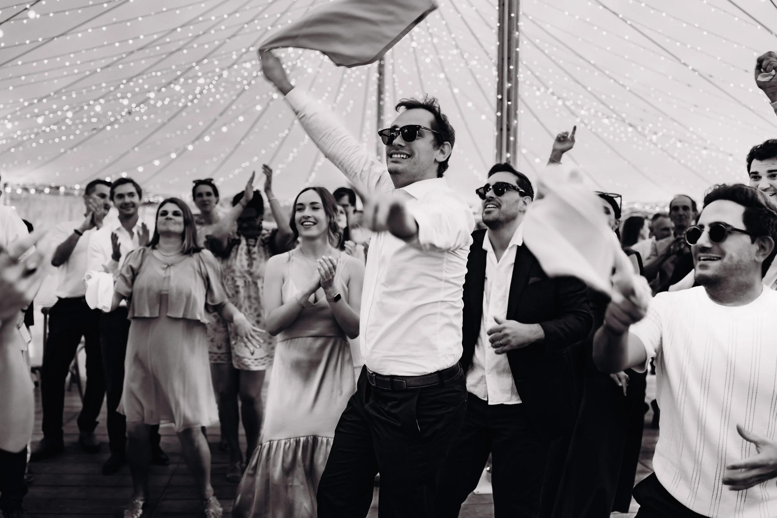 Groupe de personnes dansant et souriant sous le chapiteau de l'Orangerie des demoiselles, domaine de mariage proche de Toulouse, décoré avec un ciel étoilé, en noir et blanc.