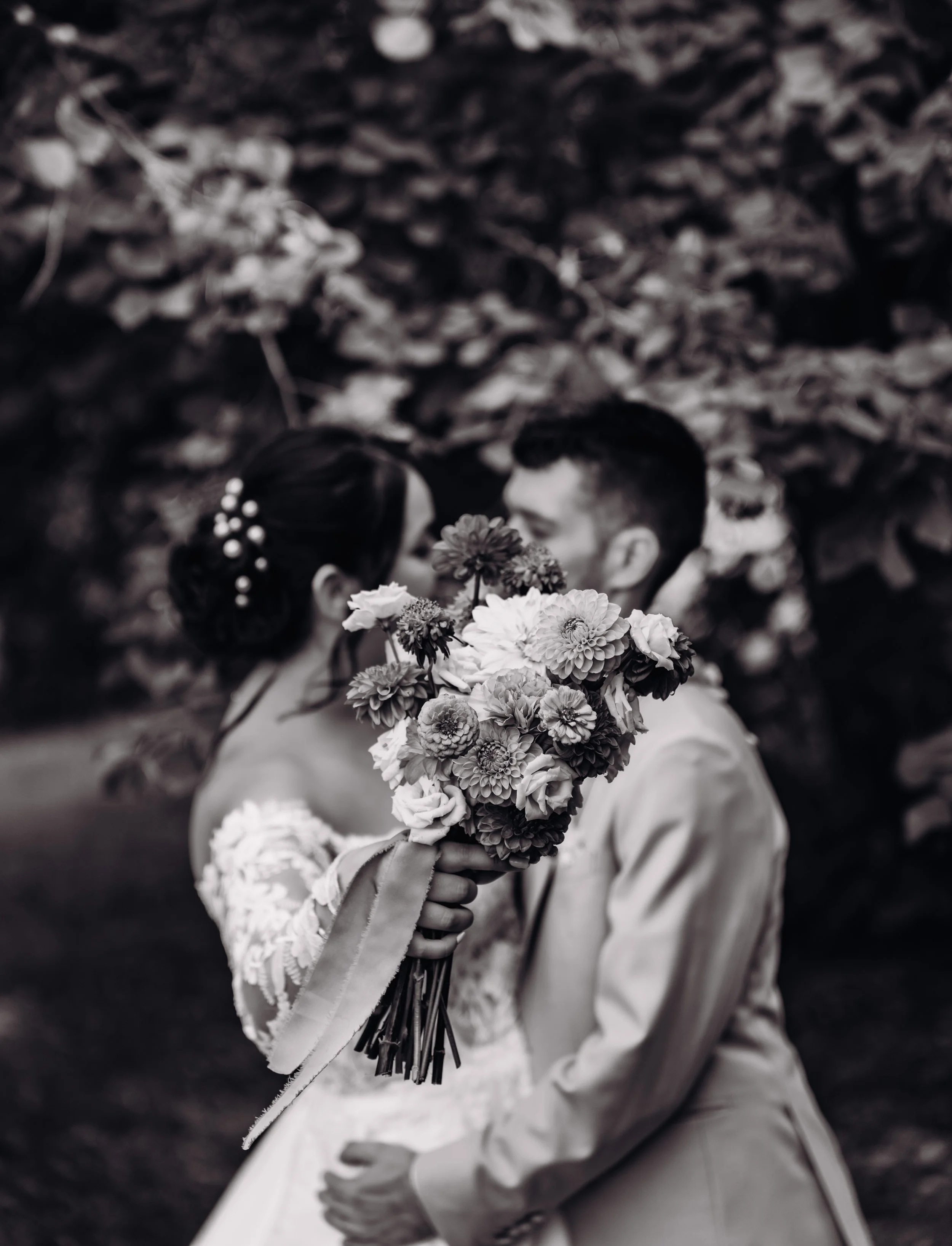 Un couple de mariés s'embrassant derrière un bouquet de fleurs lors d'une séance photo en plein air.