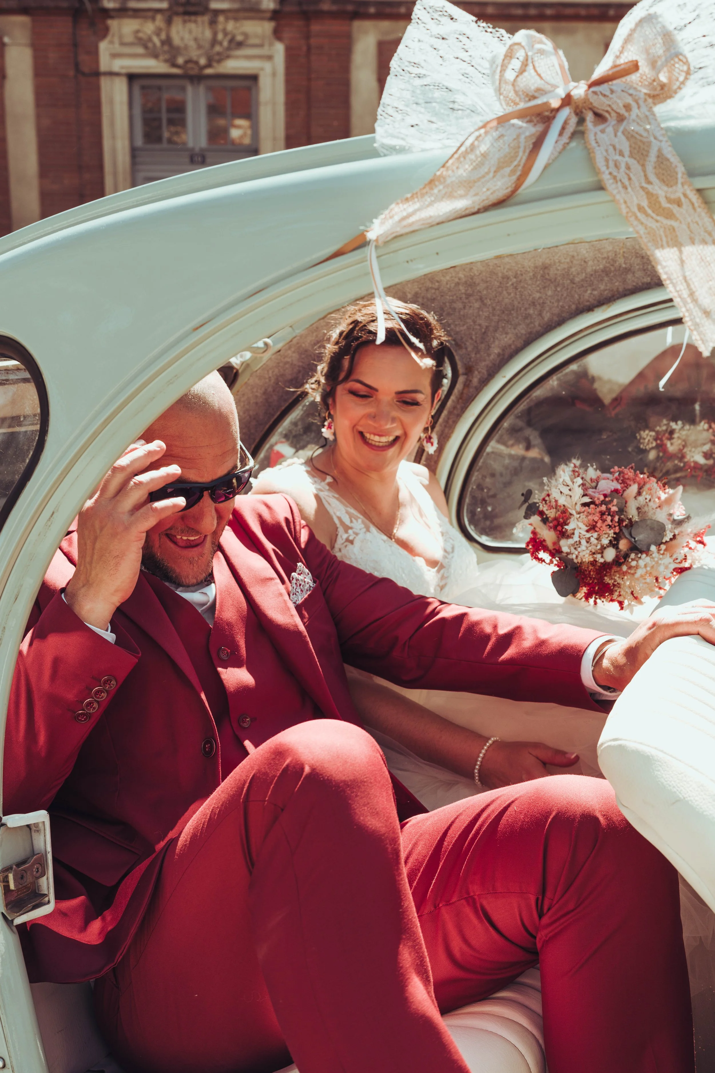 Un couple de mariés souriants dans une voiture de collection décorée en vue de leur mariage proche de Toulouse.