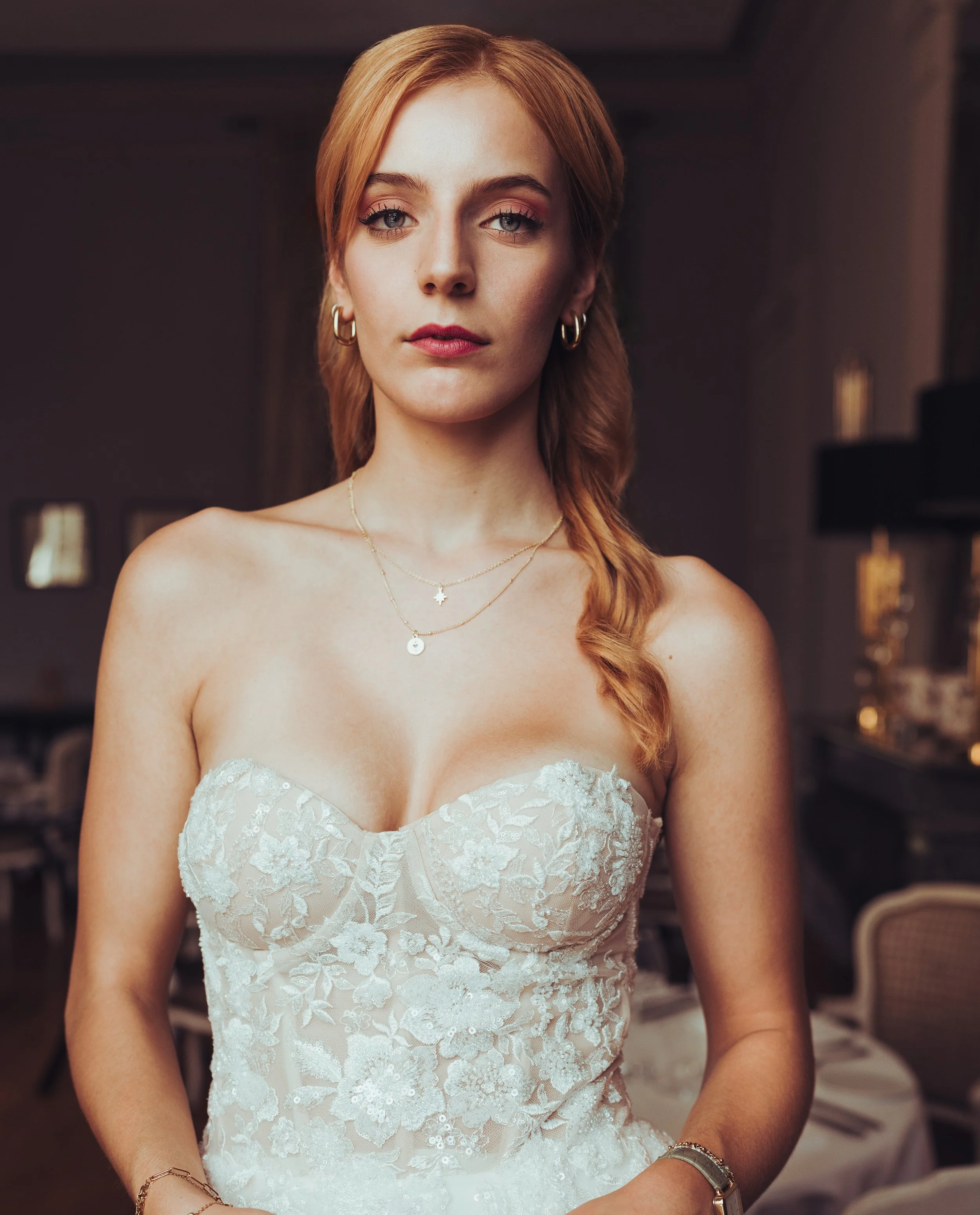 Jeune mariée portant une robe blanche en dentelle, avec des boucles d'oreilles et des colliers, dans un intérieur décoré au chateau de Drudas, proche de Toulouse.