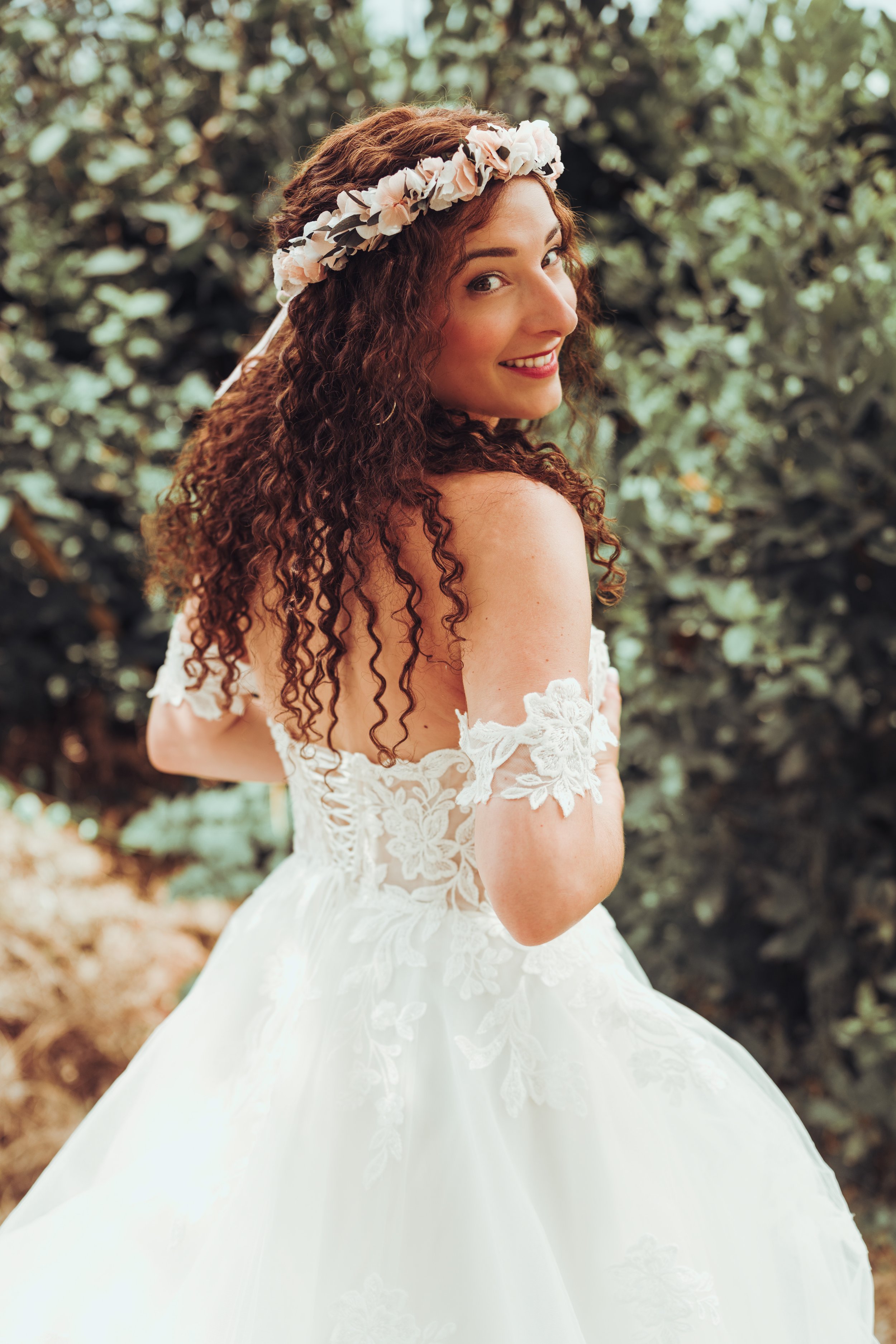 Jeune femme en robe de mariage avec couronne de fleurs, souriante, dans un jardin juste avant sa cérémonie laïque à la métairie du Fusté, proche de Toulouse. 