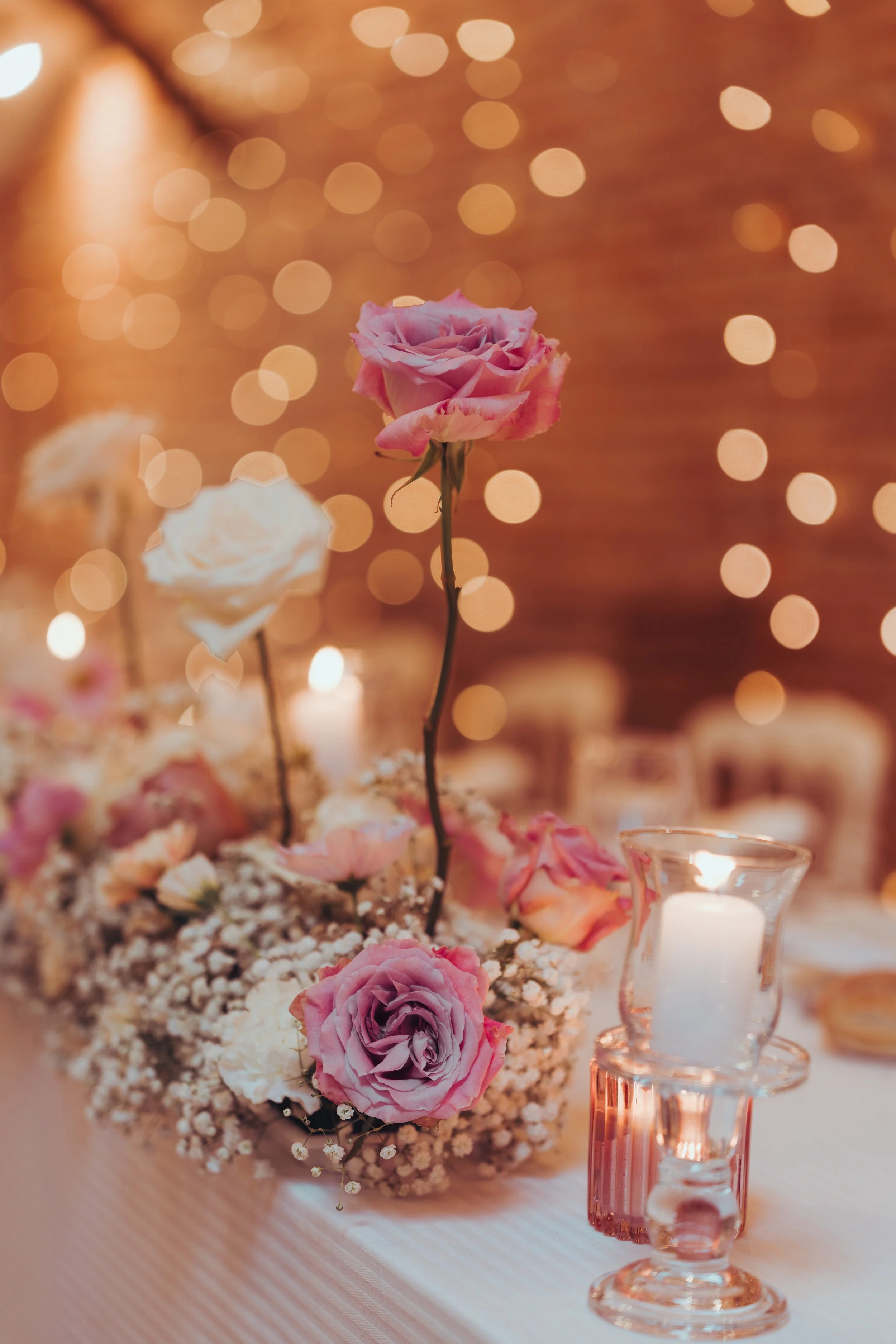 Une table décorée avec des fleurs roses et blanches, des bougies et un fond bokeh lumineux, créant une ambiance romantique au domaine de Lalanne, proche de Toulouse