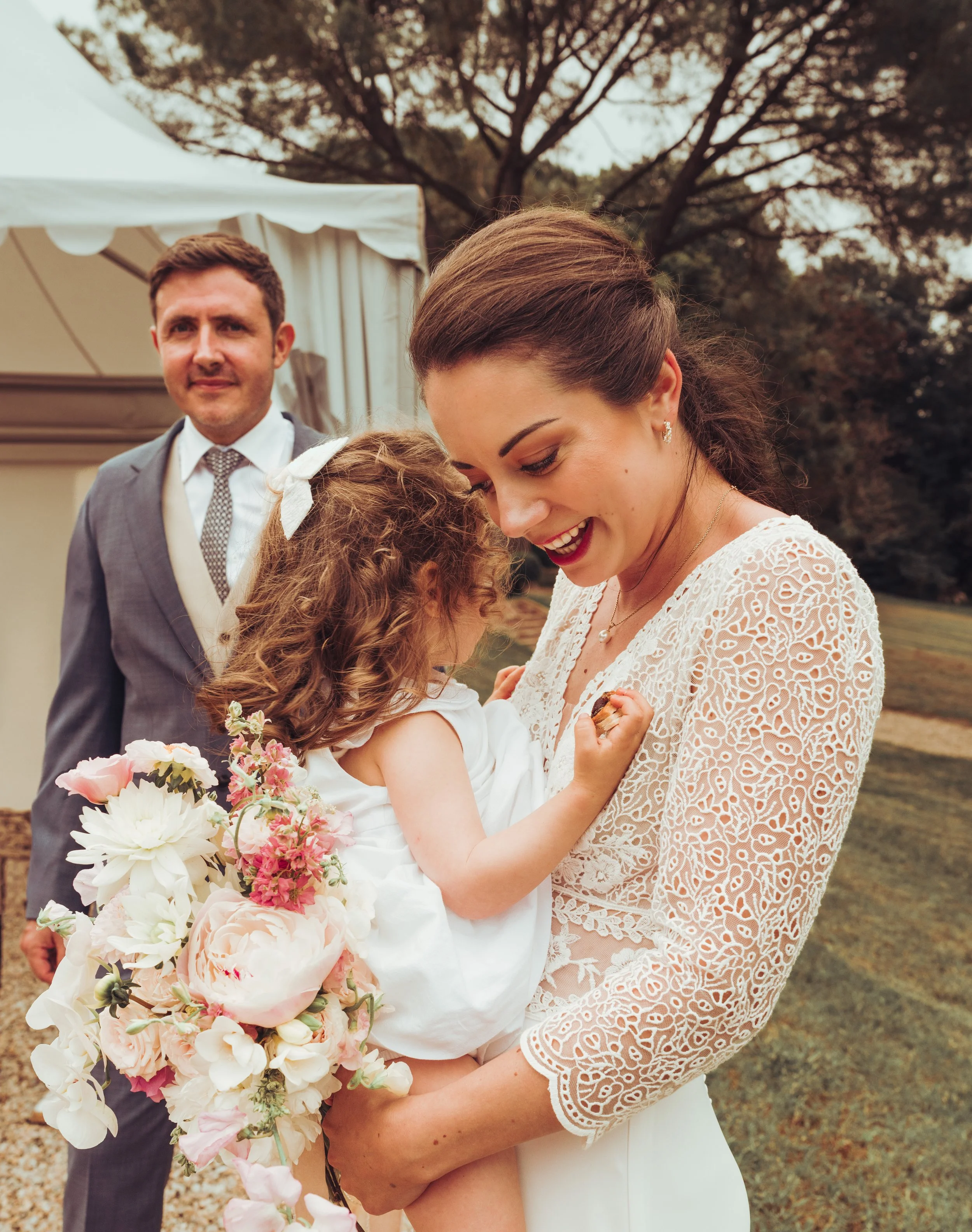 La mariée enlace sa jeune enfant sous le regard attendri du marié dans les jardins du domaine de Gailhaguet près de Toulouse, en Occitanie. 