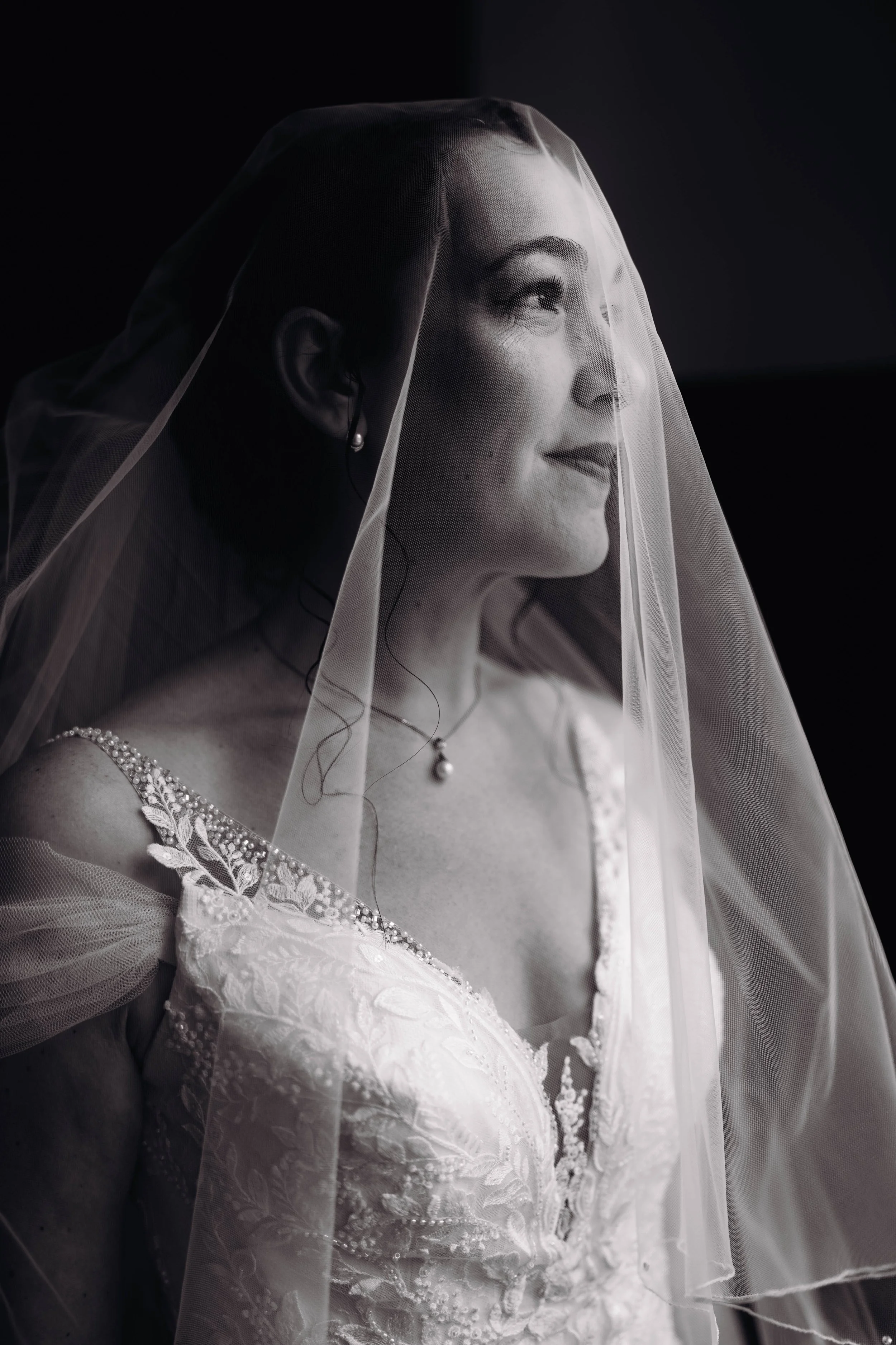 Une femme en robe de mariage et voile, souriante, en noir et blanc. Elle s'apprête à aller faire le first look avec son futur mari au château de Puydaniel près de Toulouse, en Occitanie. 