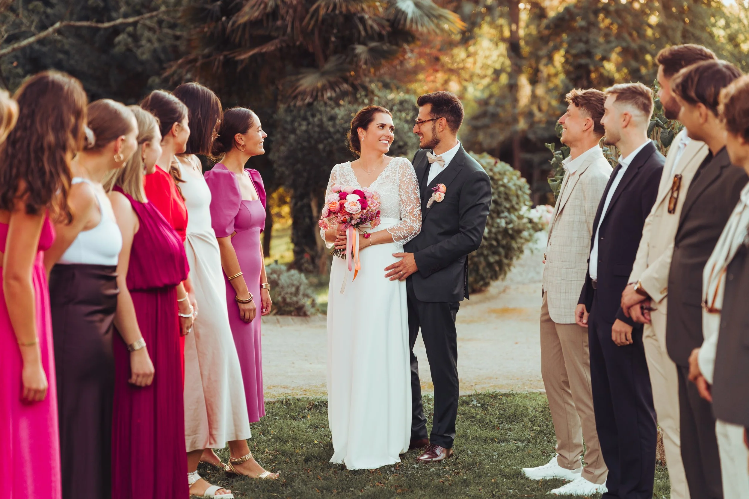 Un couple de mariés entourés d'amis lors d'un mariage en plein air au moulin de Rudelle, avec des arbres en arrière-plan, moments de bonheur et d'amour.