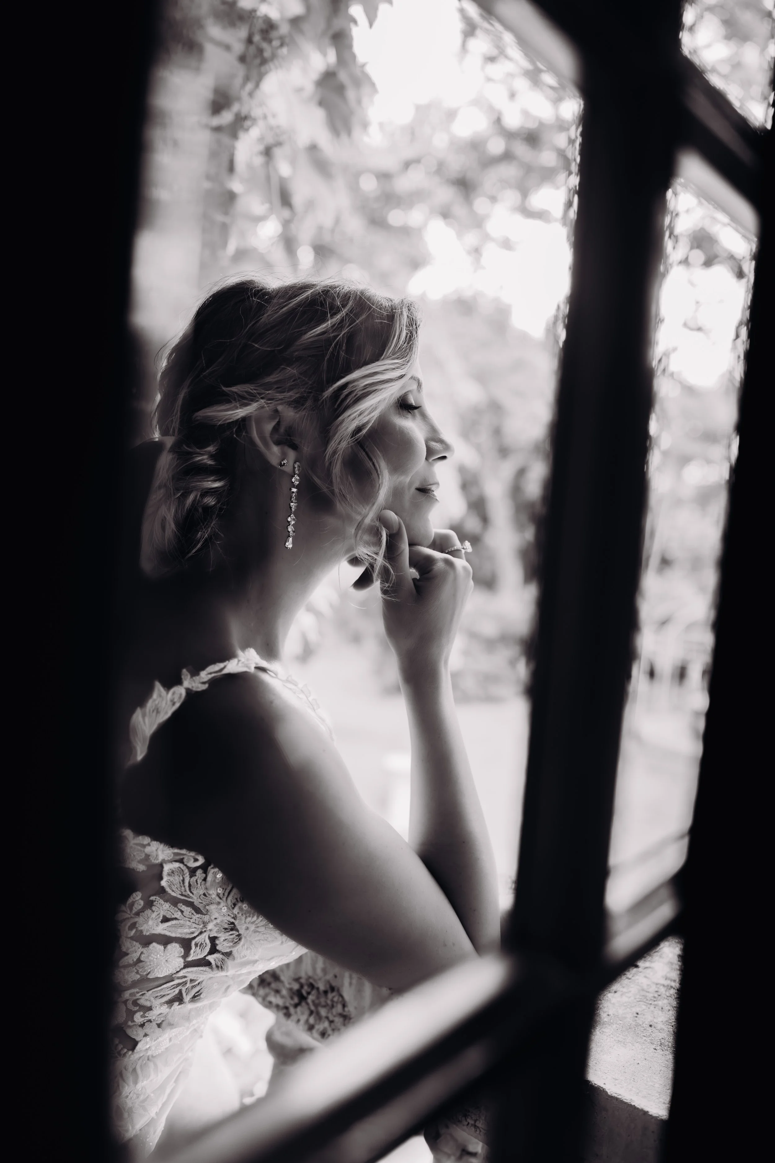 Une mariée élégante au domaine de Lalanne, regarde par une fenêtre avec une expression contemplative avant son mariage en extérieur