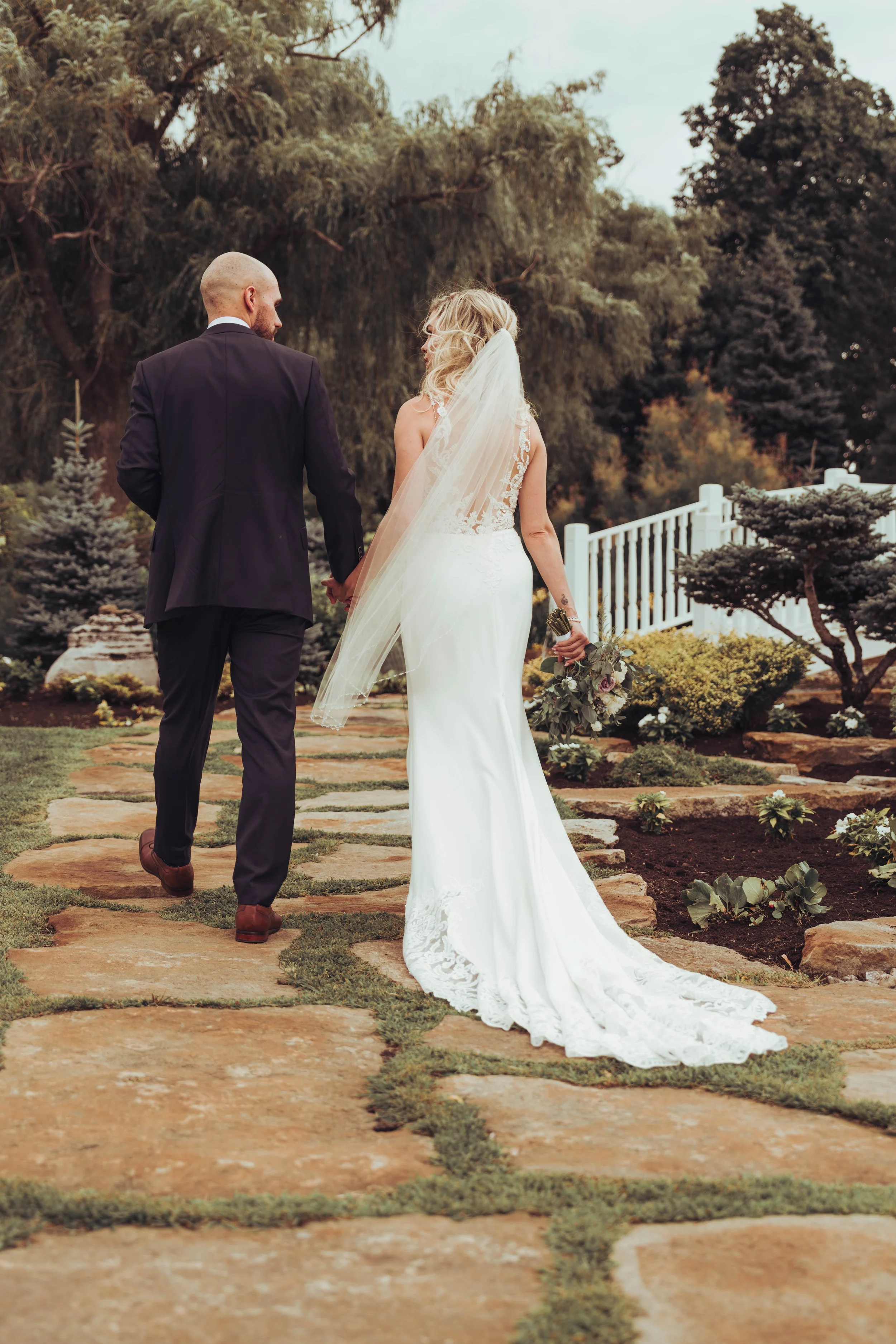 Un couple de mariés marche main dans la main sur un sentier en pierre dans les jardins du château Vaudreuil, au Canada proche de Montreal. 