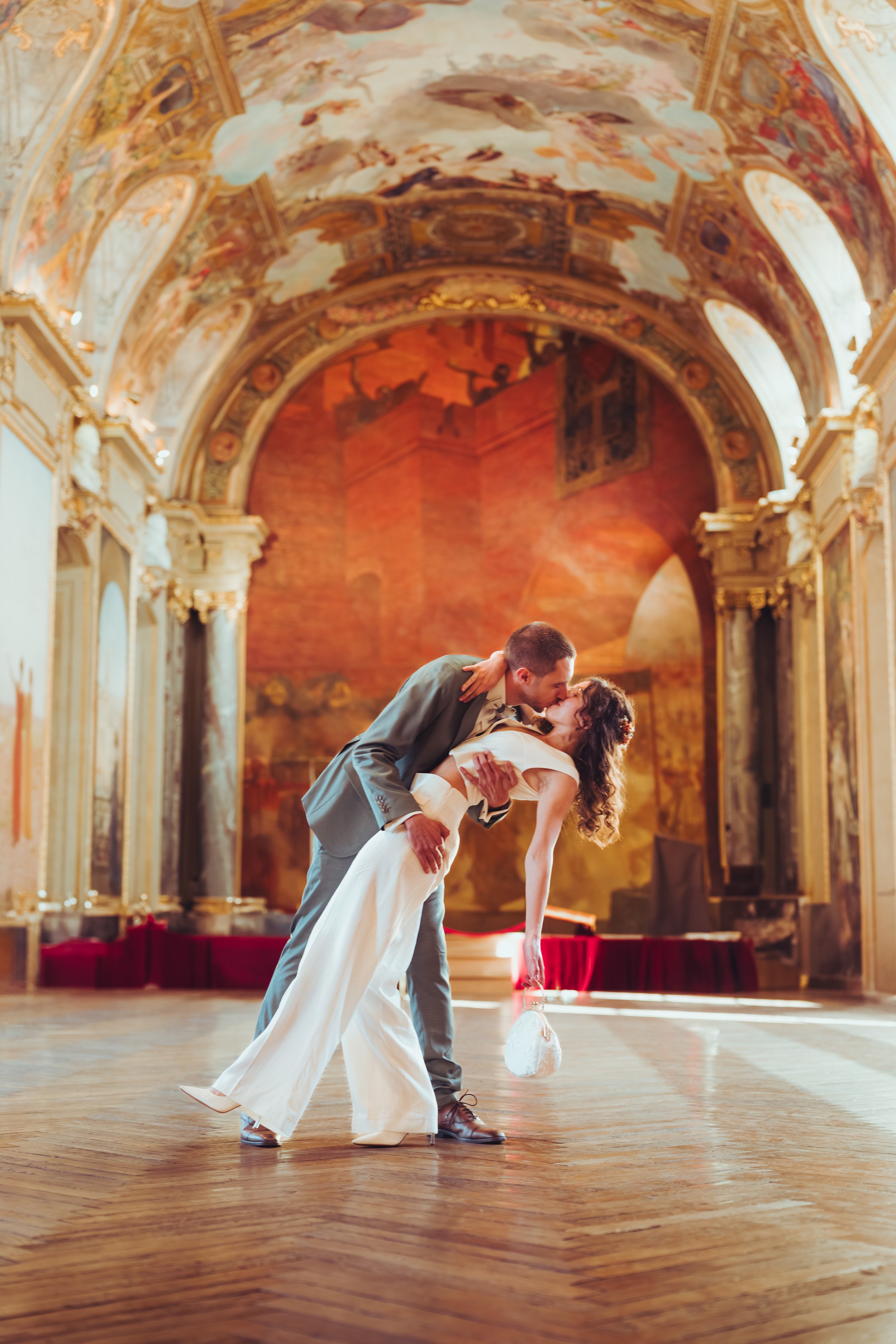 Un couple en robe de mariage et costume partage un baiser dans la salle des illustres lors de leur mariage au Capitole de Toulouse