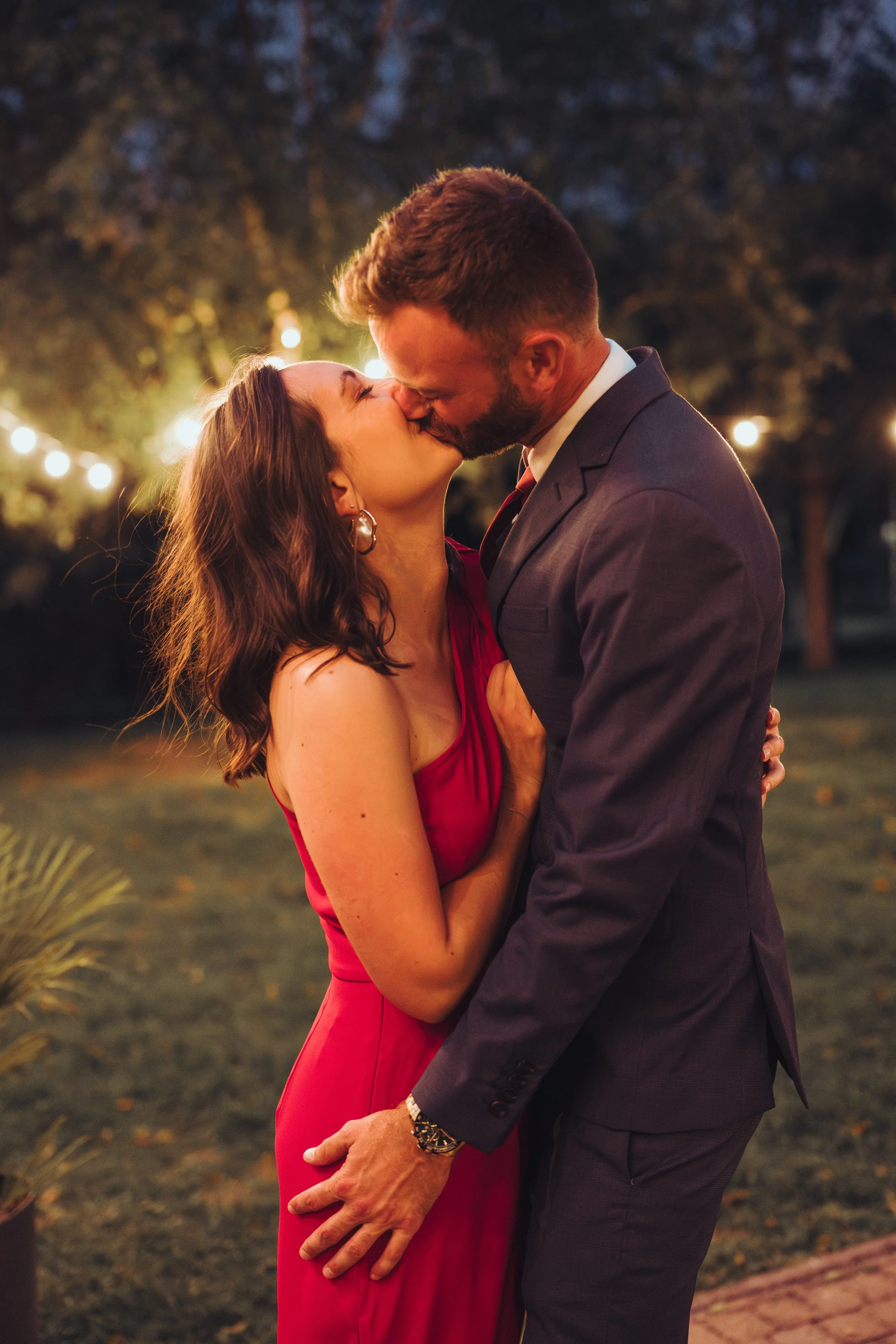 un couple qui s'embrasse lors d'une soirée romantique en plein air, avec des lumières de fête en arrière-plan