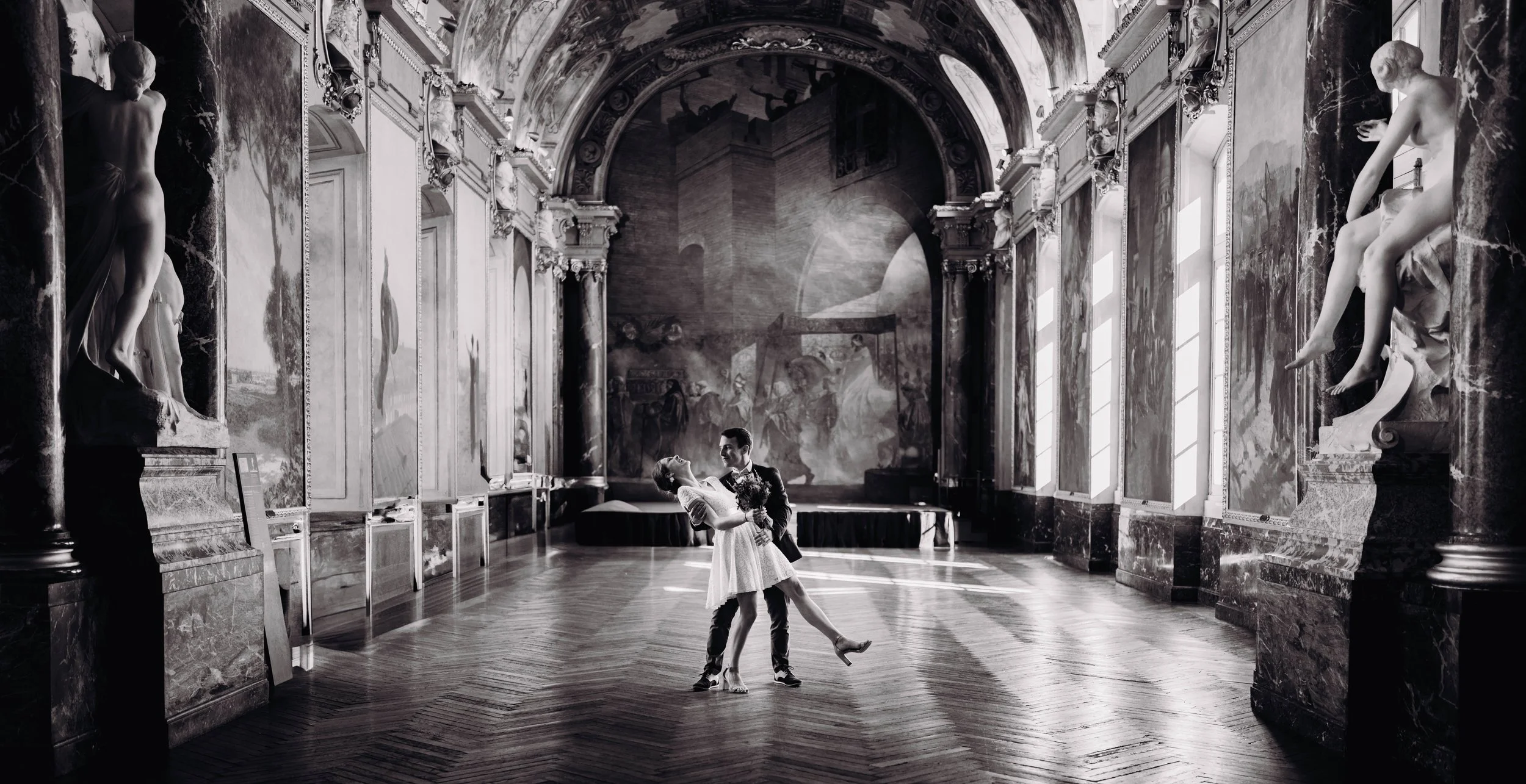 Un couple danse dans un grand hall orné de sculptures et de peintures classiques.
