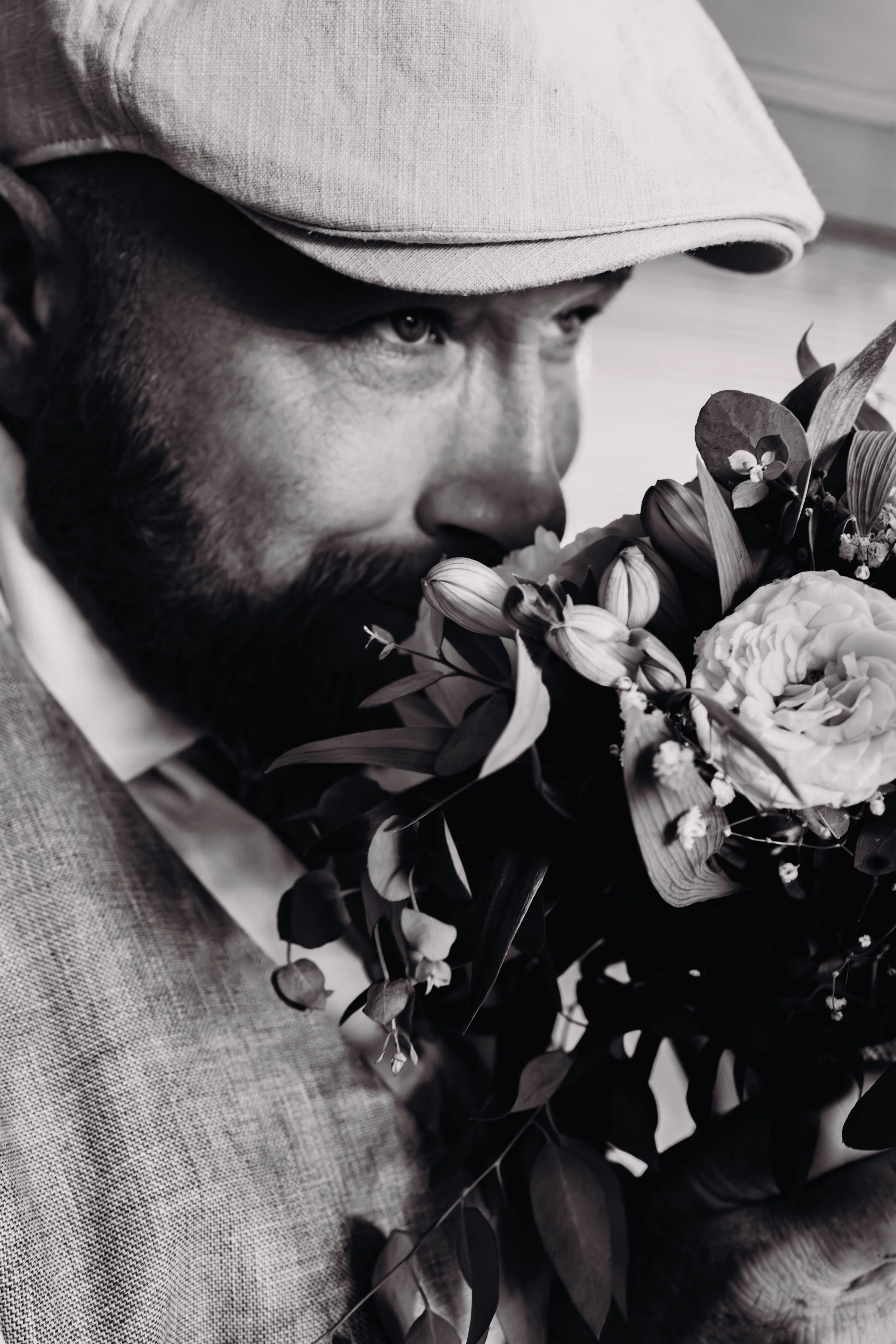 Homme portant un chapeau, avec une barbe, visage proche d'un bouquet de fleurs, en noir et blanc lors d'un mariage proche de Toulouse. 