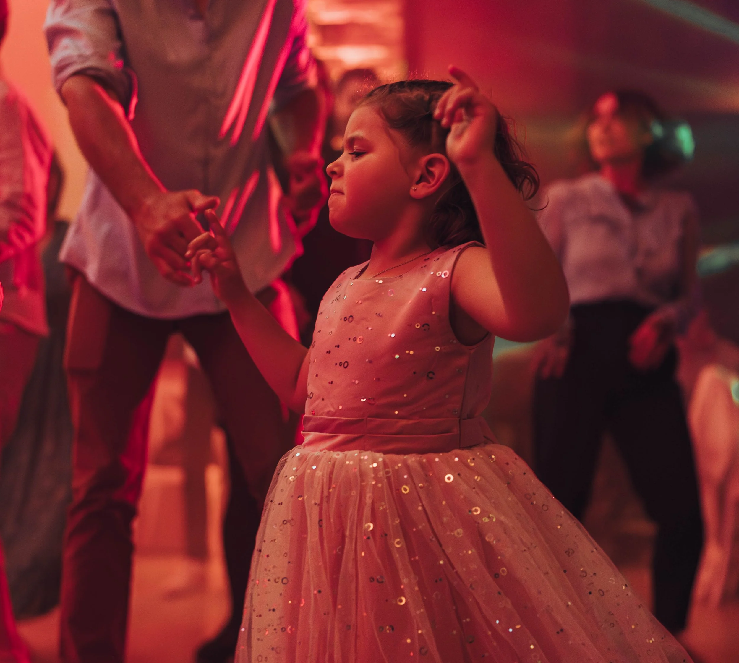 Une jeune fille danse lors d'une fête ou d'un bal de la métairie du Fusté proche de Toulouse, portant une robe rose à sequins, dans une ambiance lumineuse rouge et verte, avec d'autres personnes en arrière-plan.