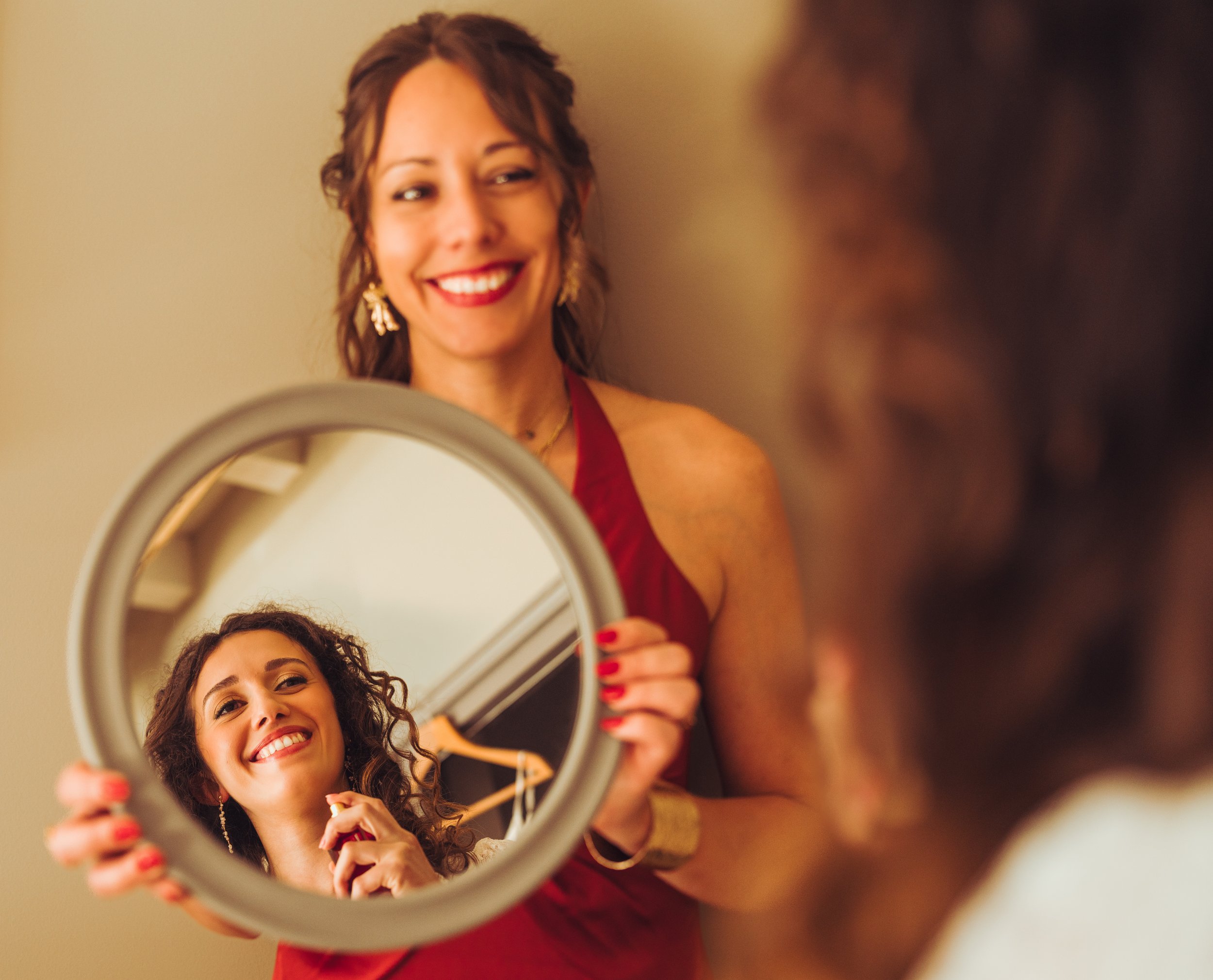 La demoiselle tient un miroir rond pour permettre à la mariée quelques retouches maquillage avant sa cérémonie laïque en plein air dans les sublimes jardin à la français du domaine de Gailhaguet, proche de Toulouse.