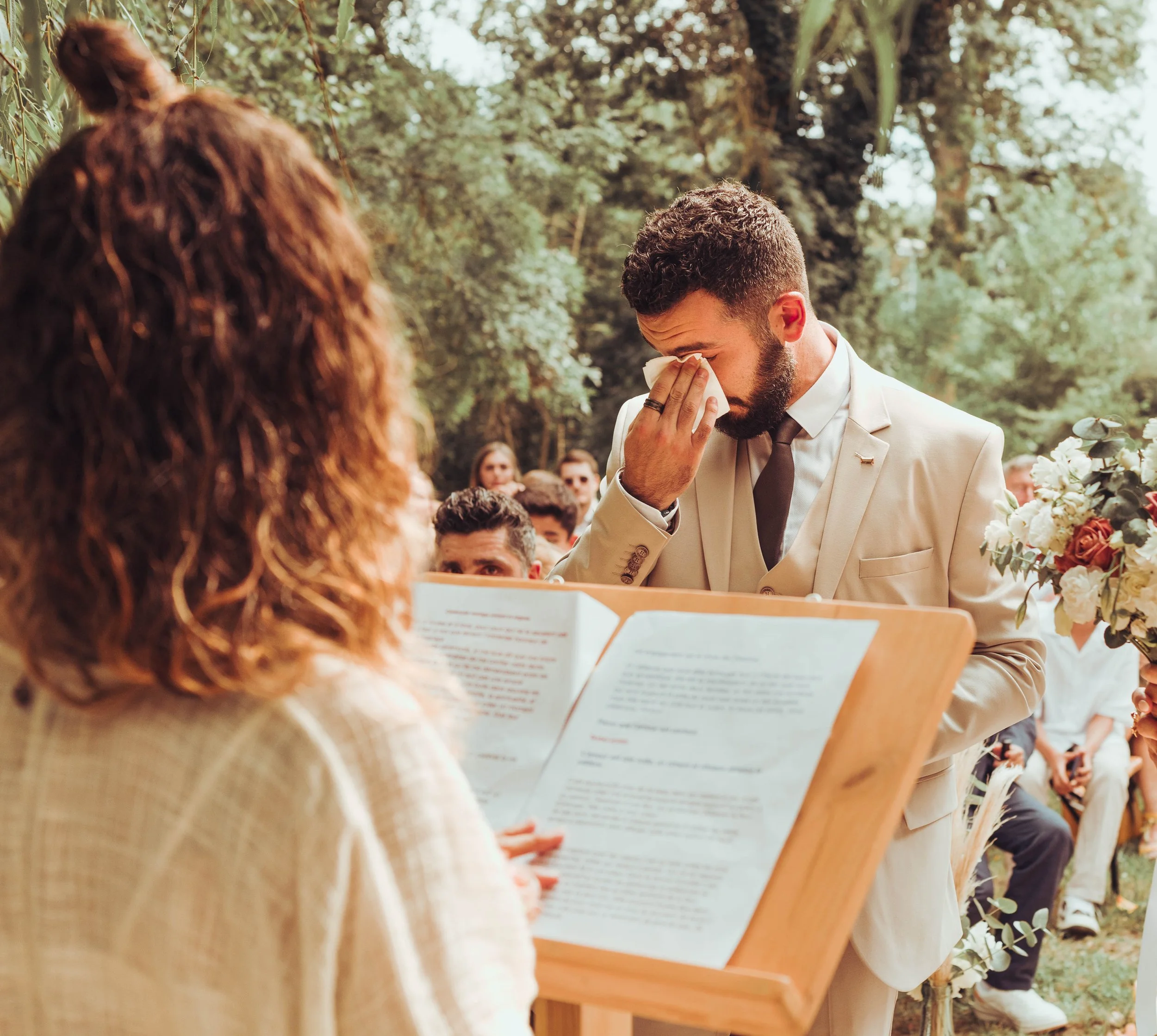Le marié ému pleure, tenant un mouchoir dans une main, lors de sa cérémonie laïque de mariage en plein air, sous des arbres au moulin de Rudelle 
