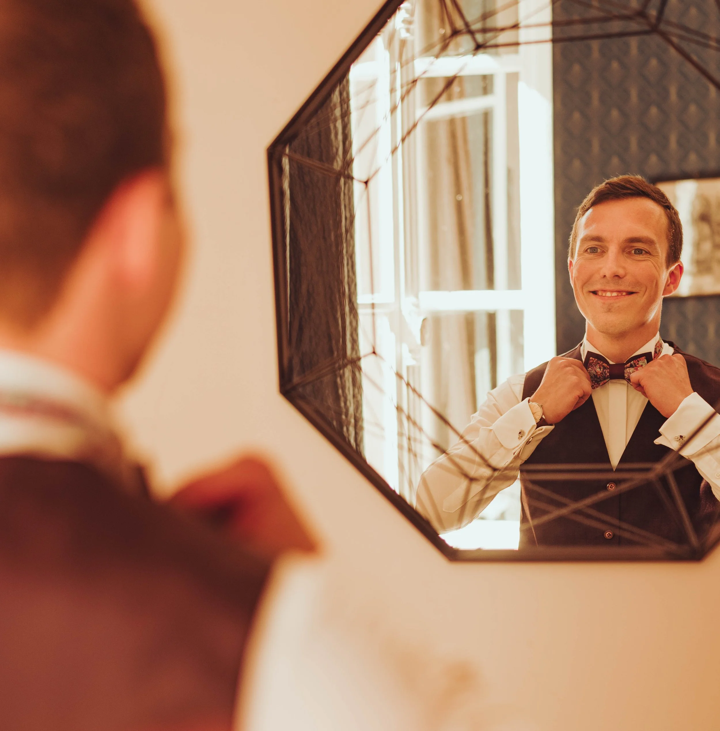 Le marié souriant ajuste un nœud papillon devant un miroir au manoir du Thouron près de Toulouse, en Occitanie. 