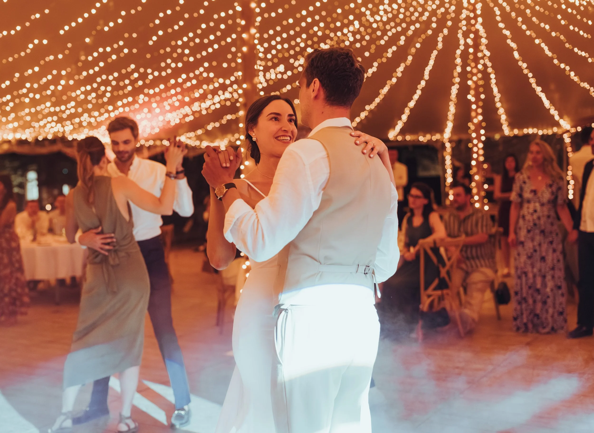Ouverture de bal par les mariés lors de leur mariage sous le grand chapiteau de l'Orangerie des demoiselles décoré de guirlandes lumineuses, entouré de leurs proches
