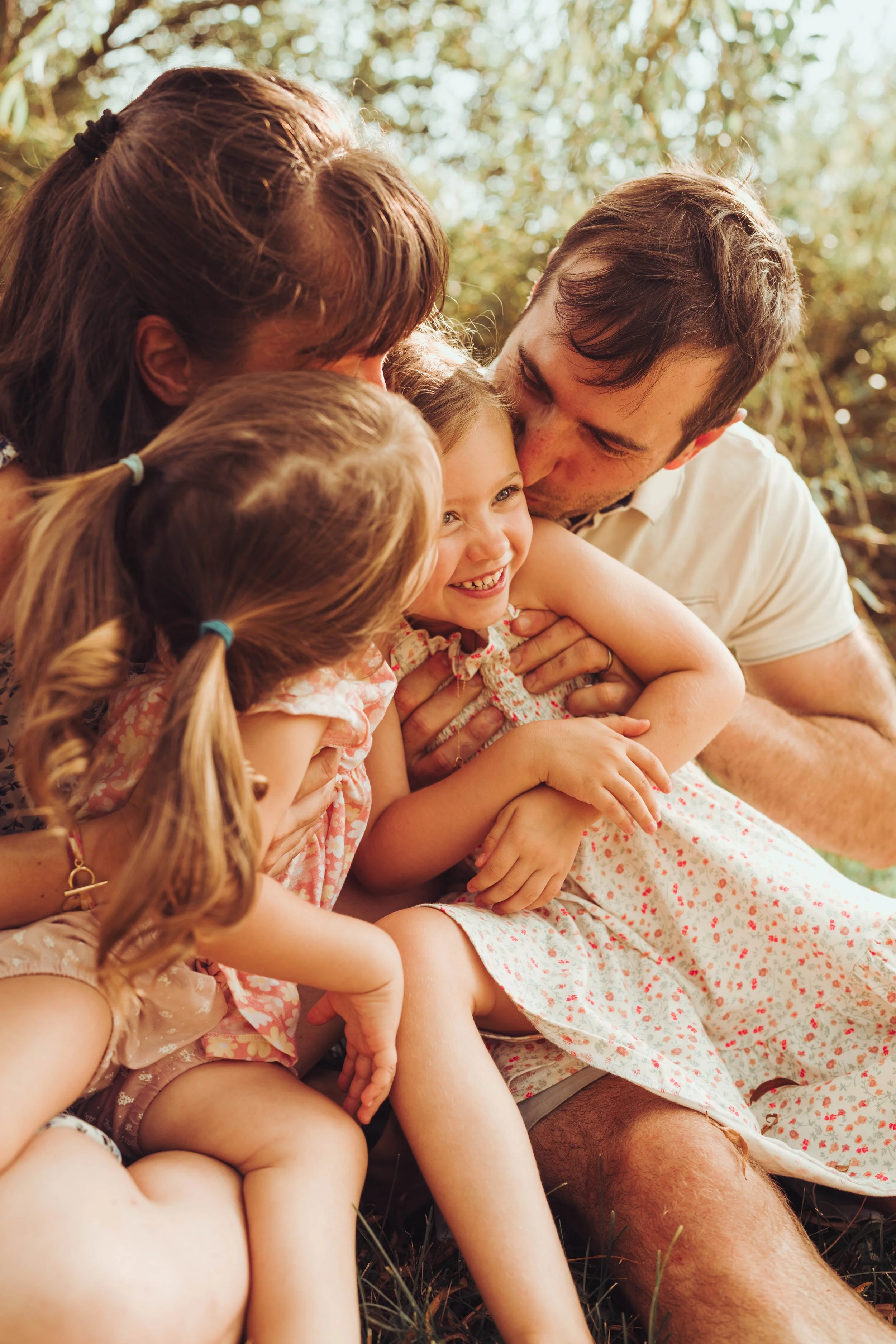 Une famille de quatre personnes, deux adultes et deux jeunes filles, partage un moment de joie en extérieur dans la nature, tous souriants et s'étreignant chaleureusement.