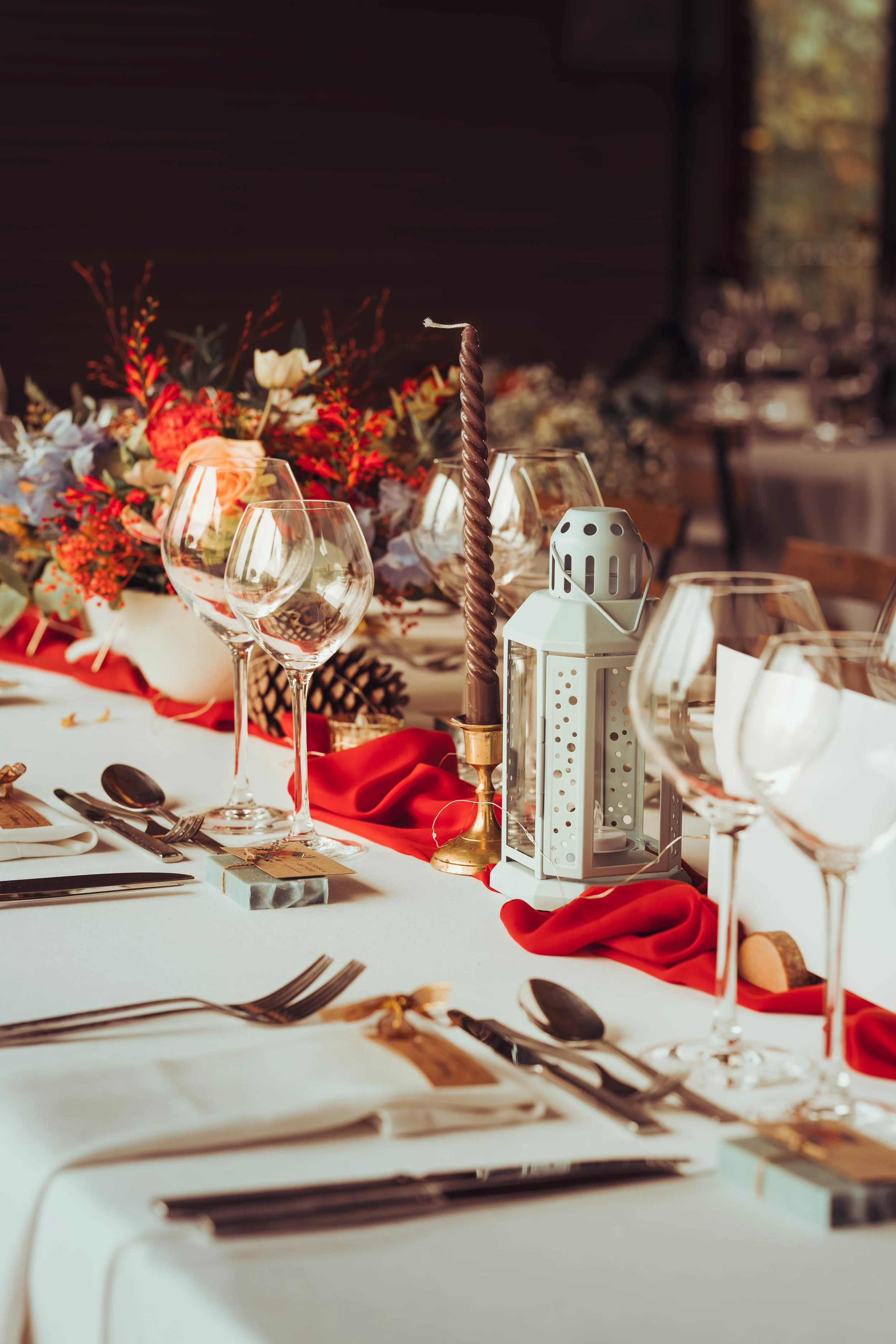 Table de mariage préparée avec des verres à vin, une lanterne, une bougie torsadée, et un décor floral avec des couleurs chaudes, au domaine de Gailhaguet proche de Toulouse. 