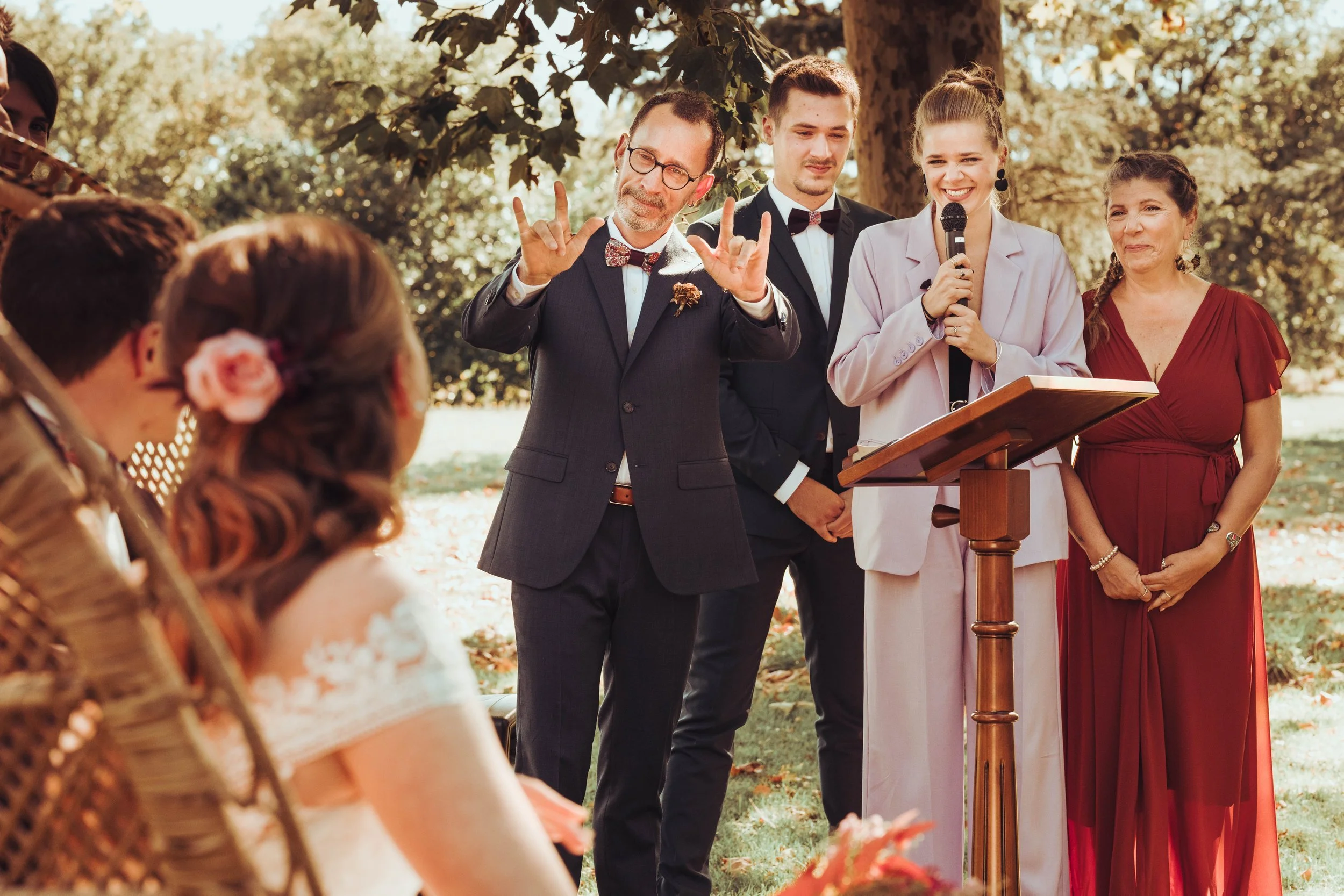 Discours de mariage par le père malentendant de la mariée au manoir du Thouron proche de Toulouse, entouré de quatre personnes en tenue formal, devant un public, sous un arbre en automne.